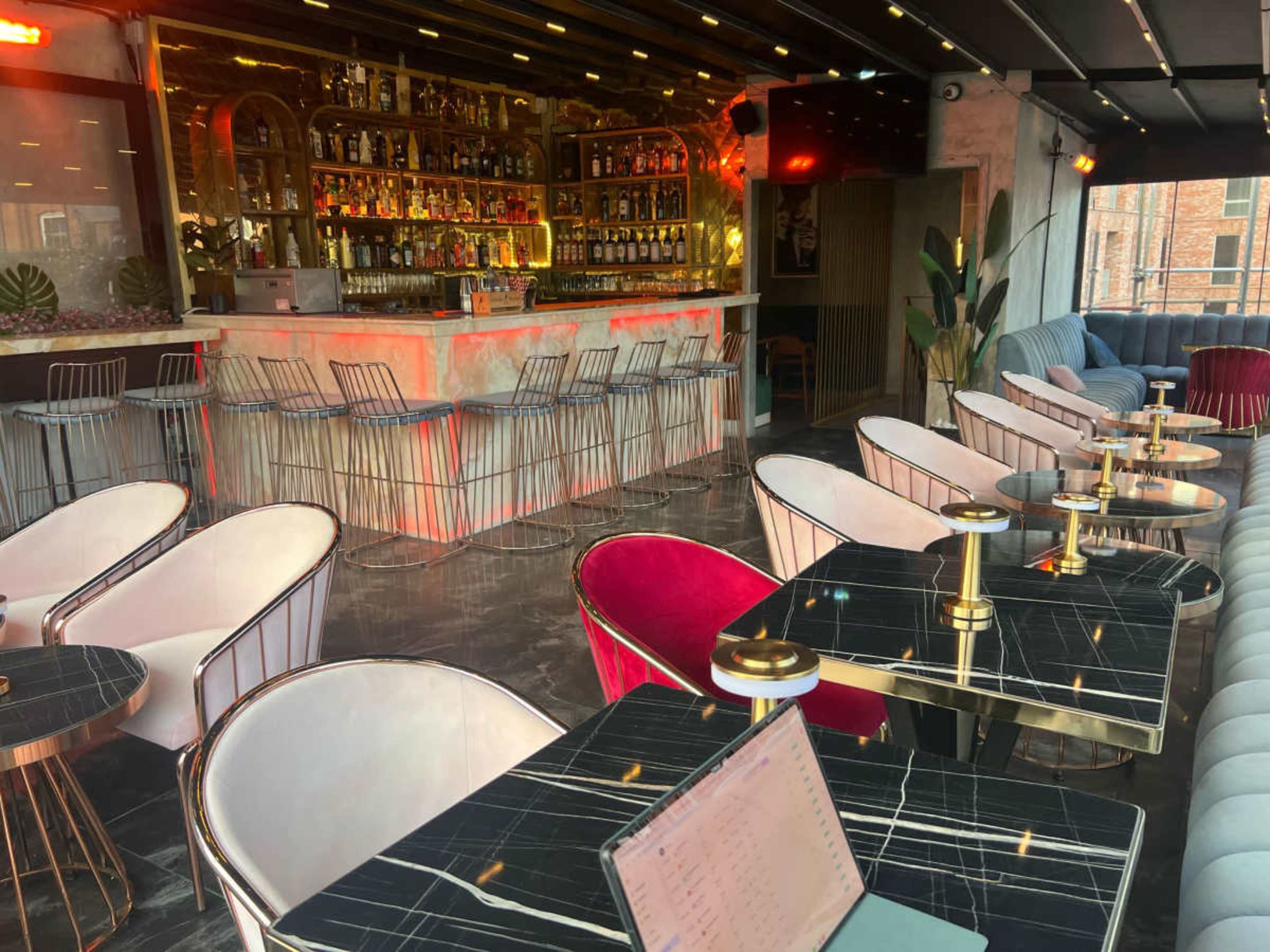 The image shows a modern lounge bar with stylish seating, a polished bar area filled with various bottles, and elegant tables arranged throughout the space.