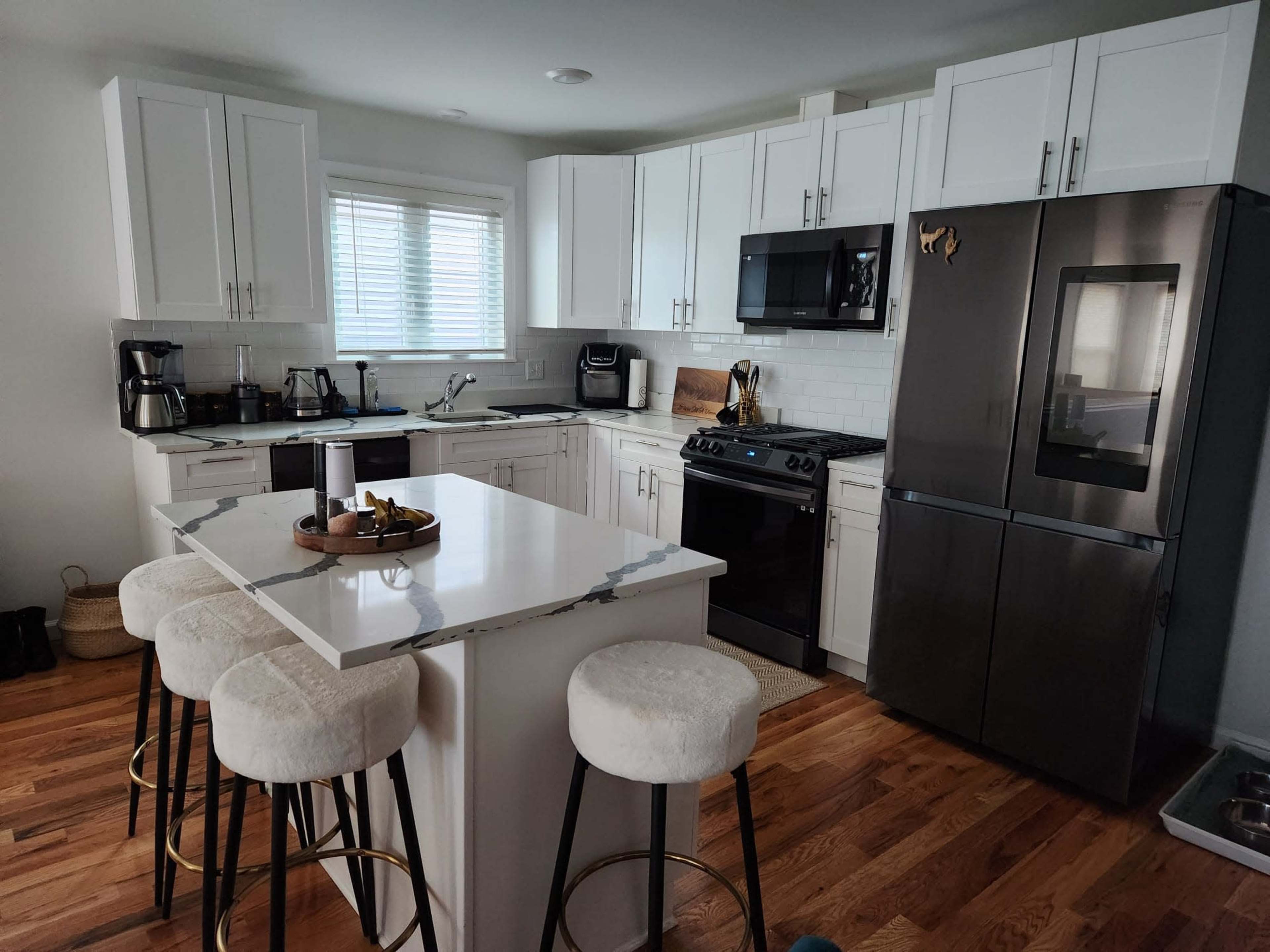 A modern kitchen with white cabinets, a dark refrigerator, a black stove, and a central island with four bar stools.