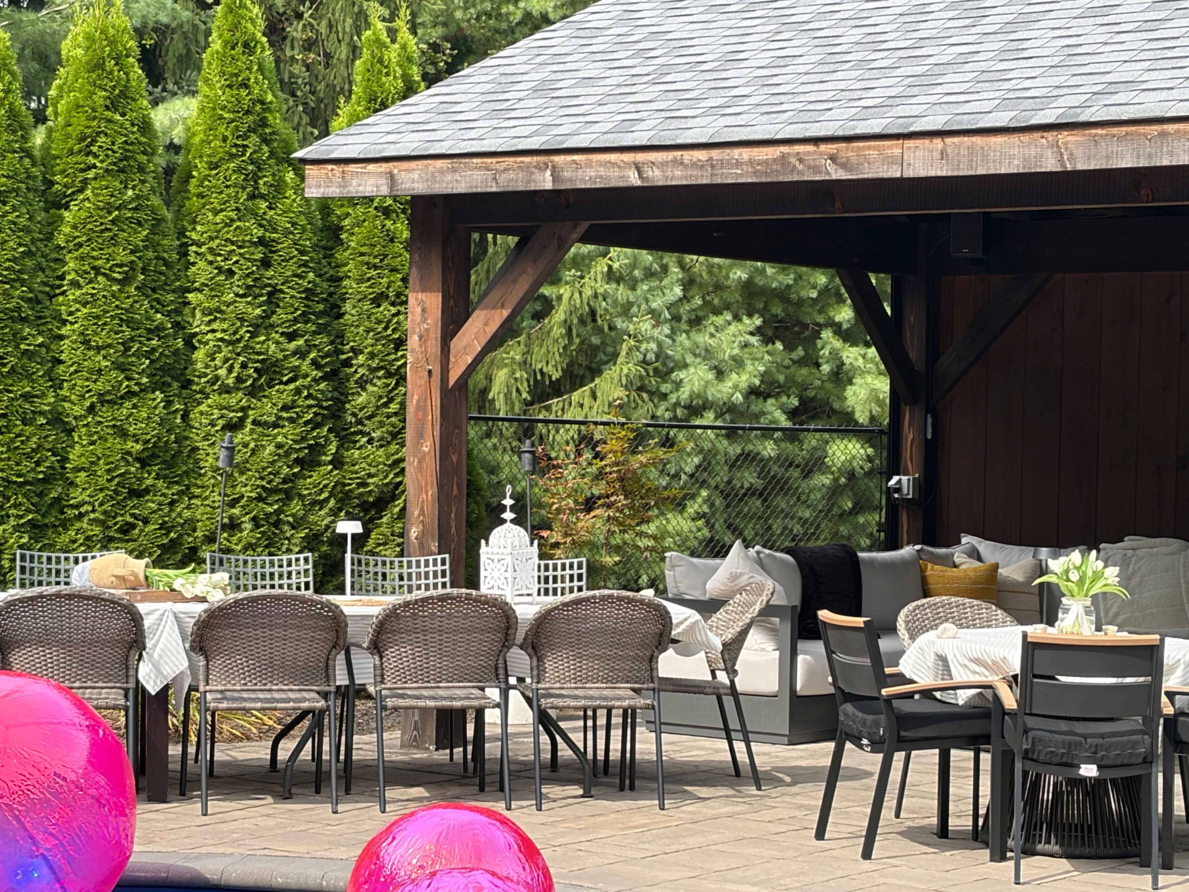 A covered outdoor space features a long dining table set with chairs and a lounge area with upholstered seating.