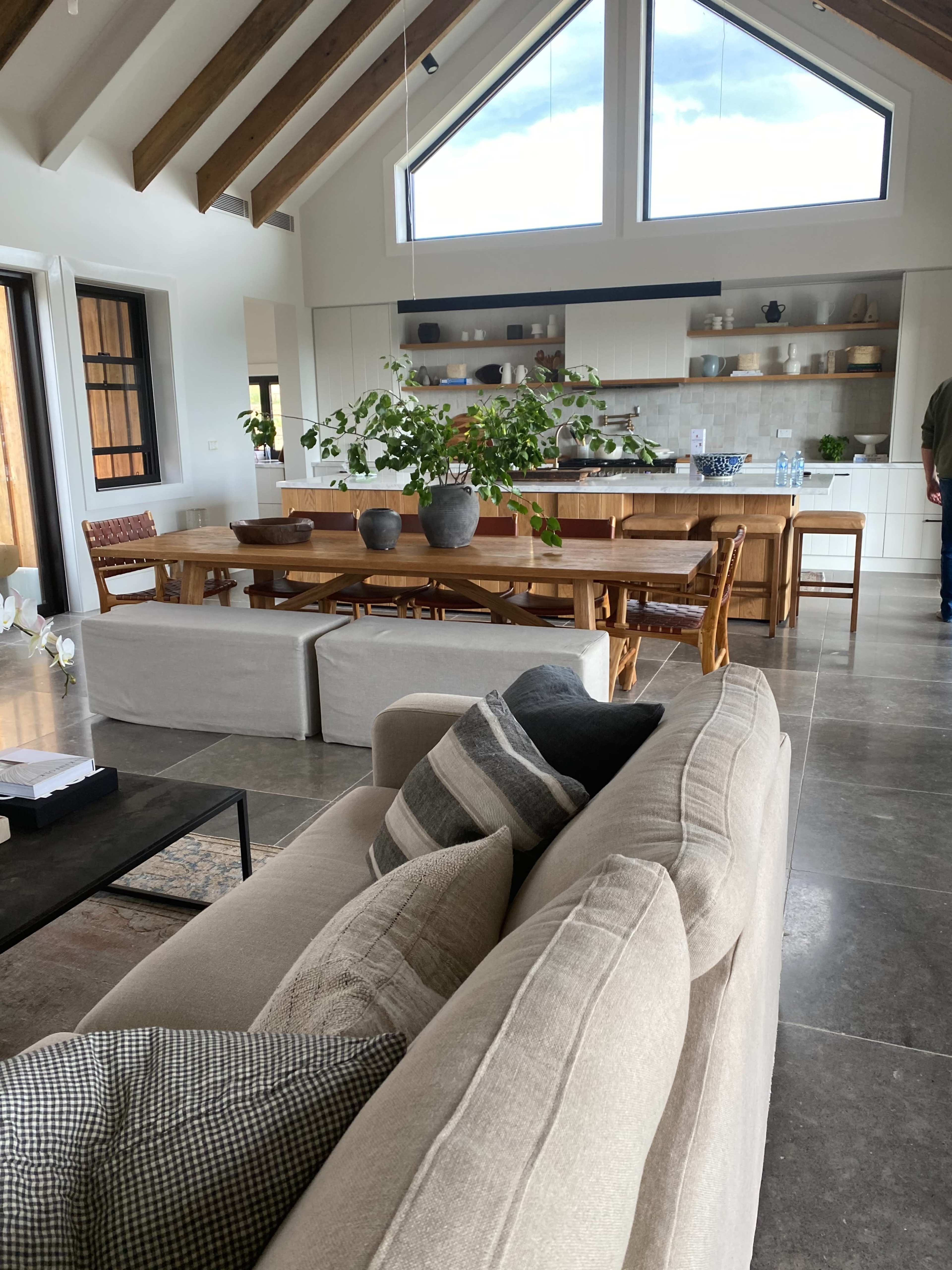 A spacious living area with a large kitchen and dining table, featuring high ceilings and multiple large windows.