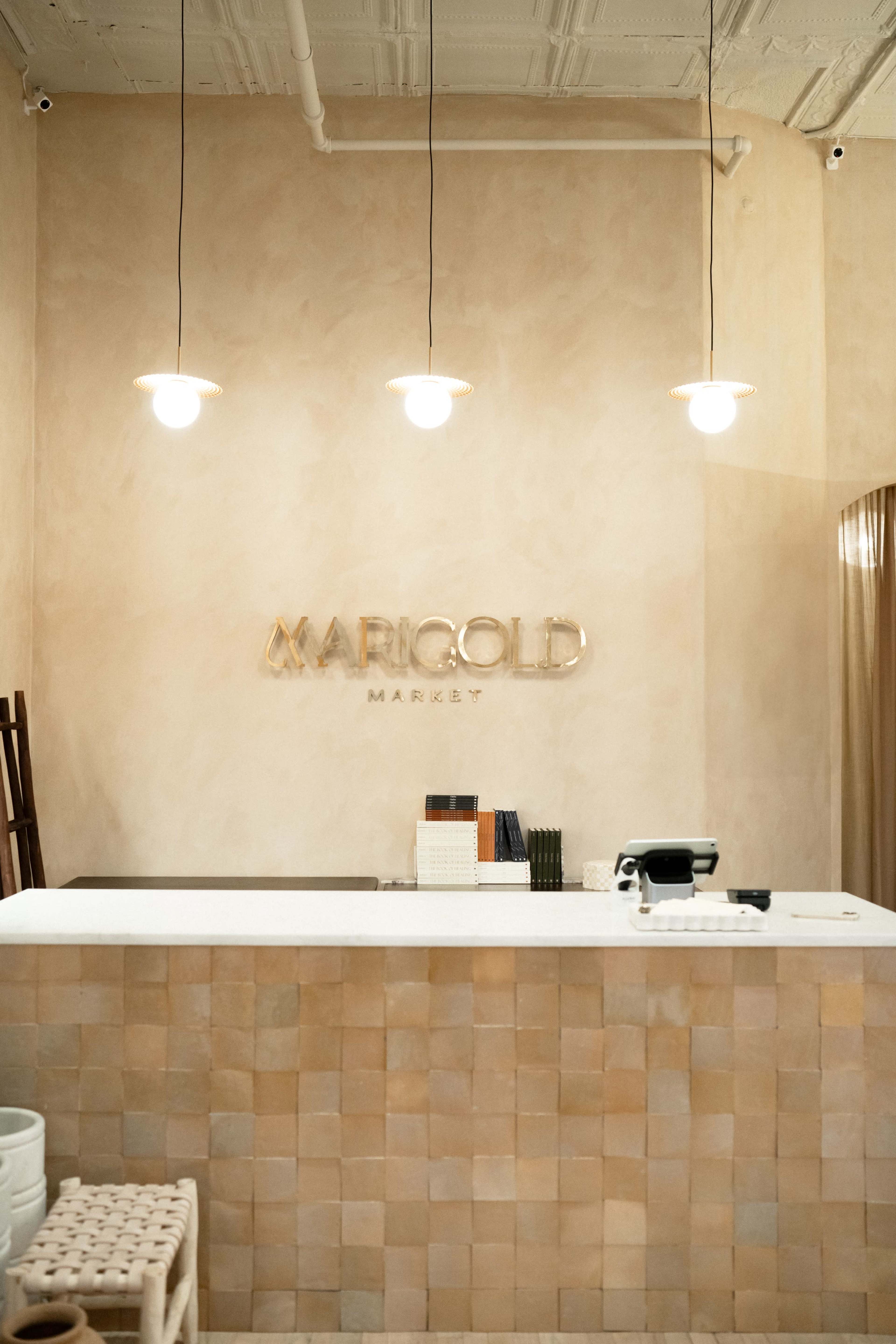 The image shows a reception area with a light-colored wall featuring the name "MARIGOLD MARKET" and a white service counter with warm-toned lighting above.