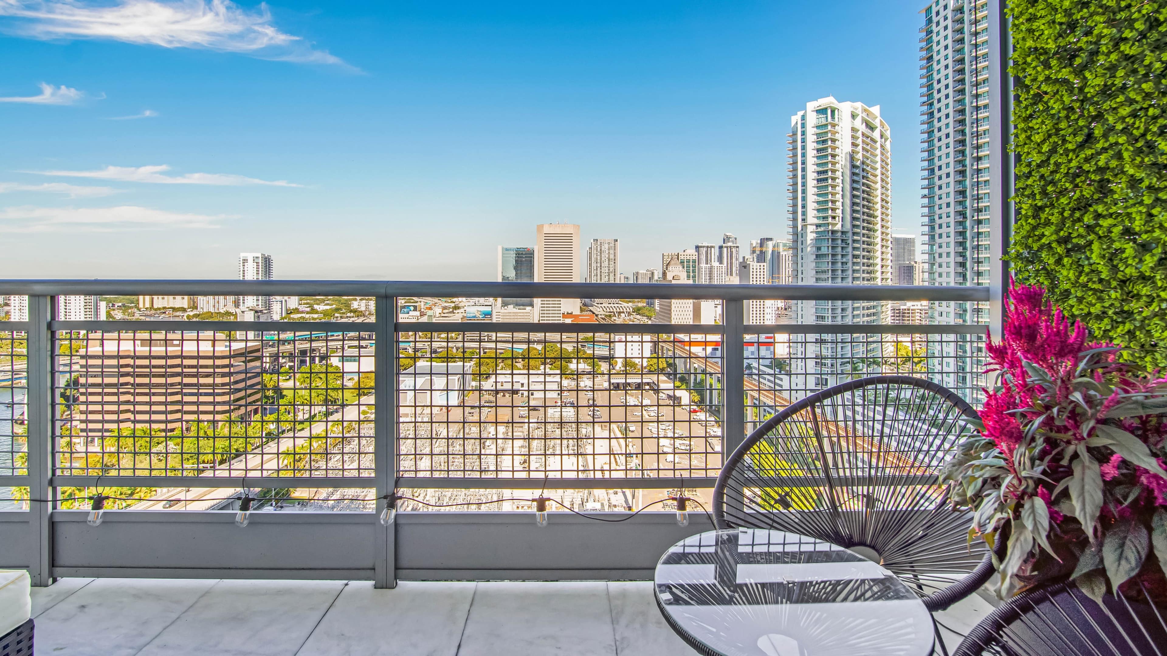 A balcony with modern furniture overlooks a city skyline featuring high-rise buildings under a clear sky.