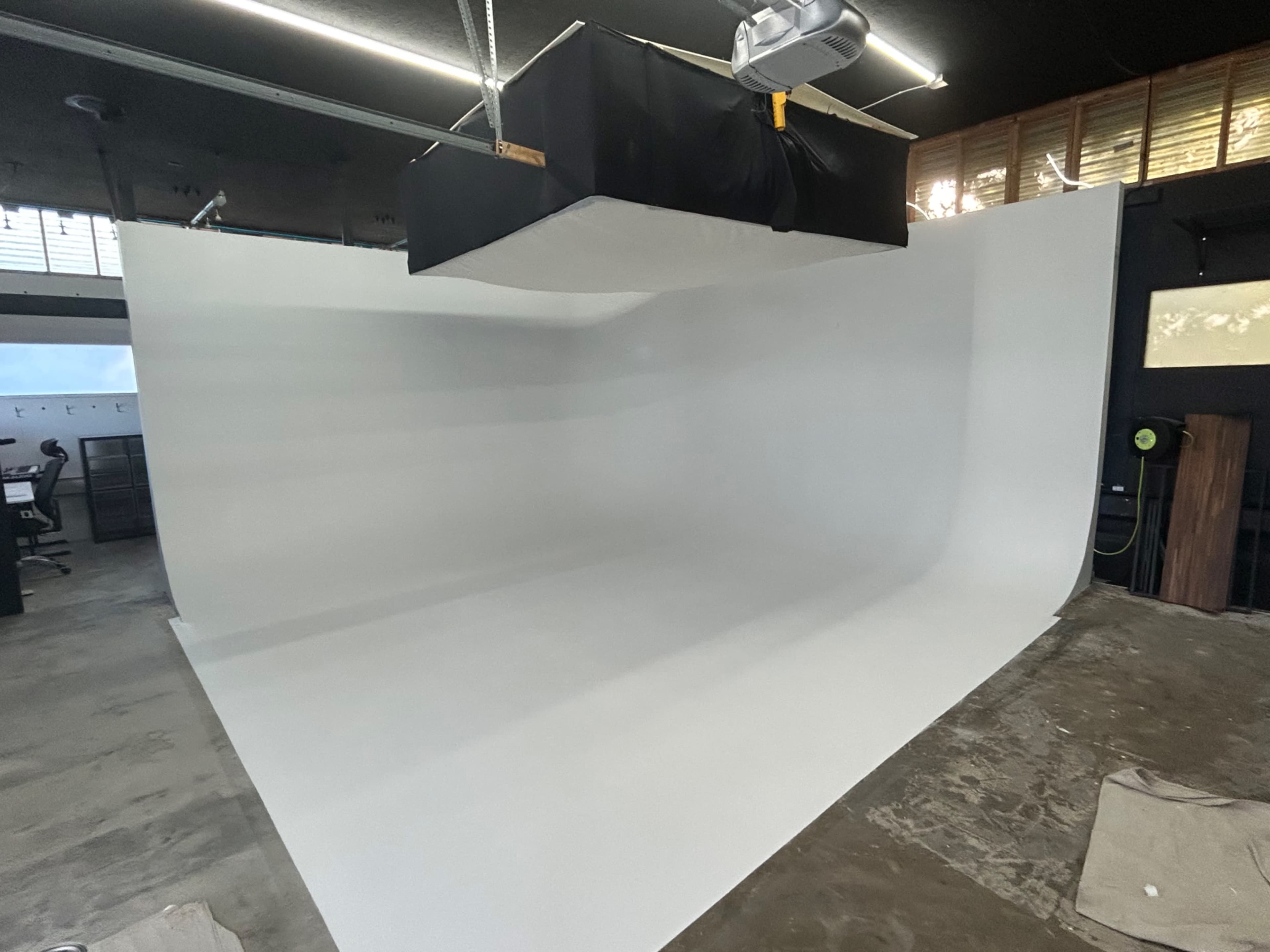 The image shows a photography studio with a white backdrop and a suspended lighting setup overhead.