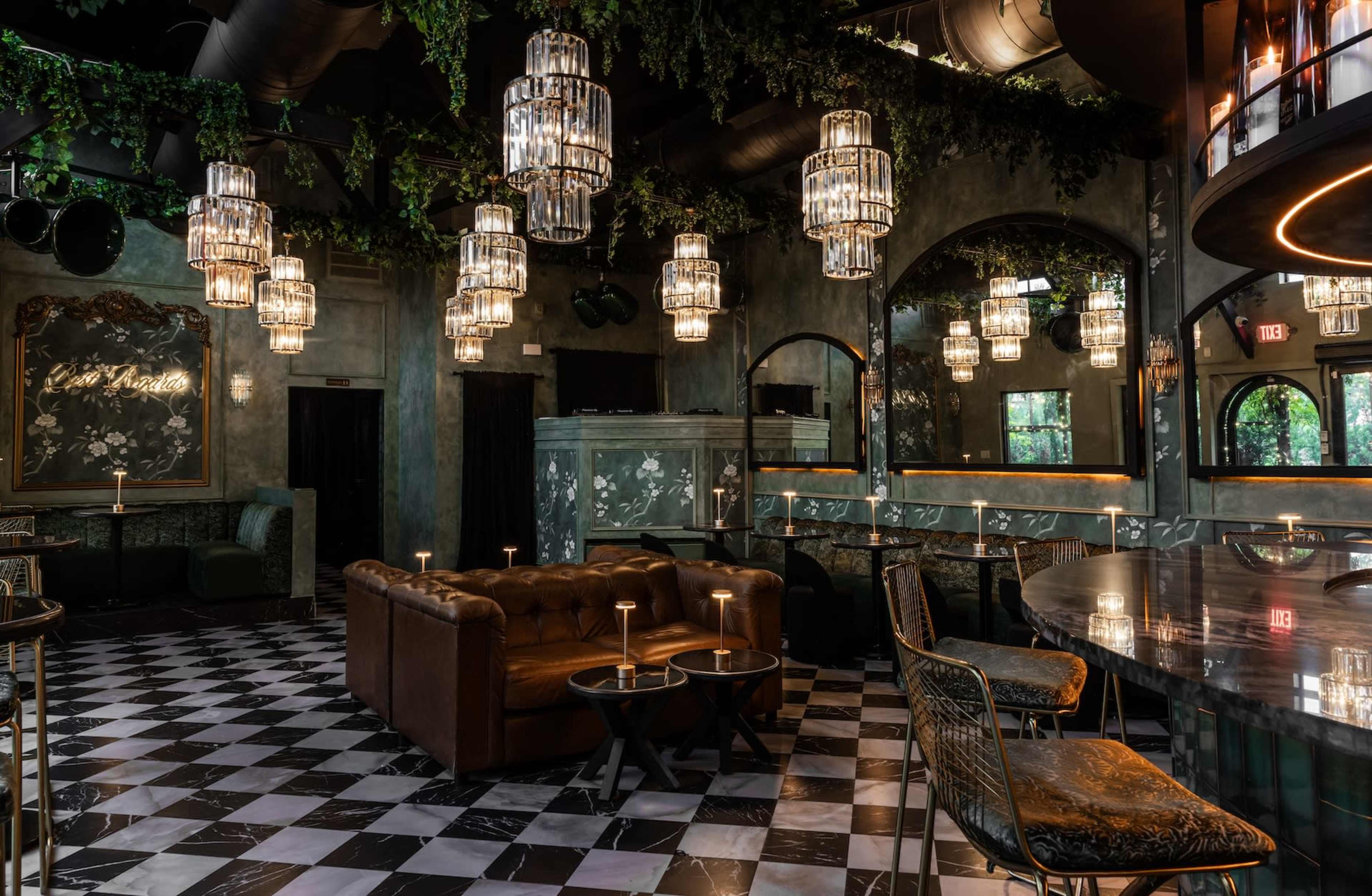 The image shows a dimly lit lounge with a checkerboard floor, plush seating, and decorative chandeliers hanging from the ceiling.