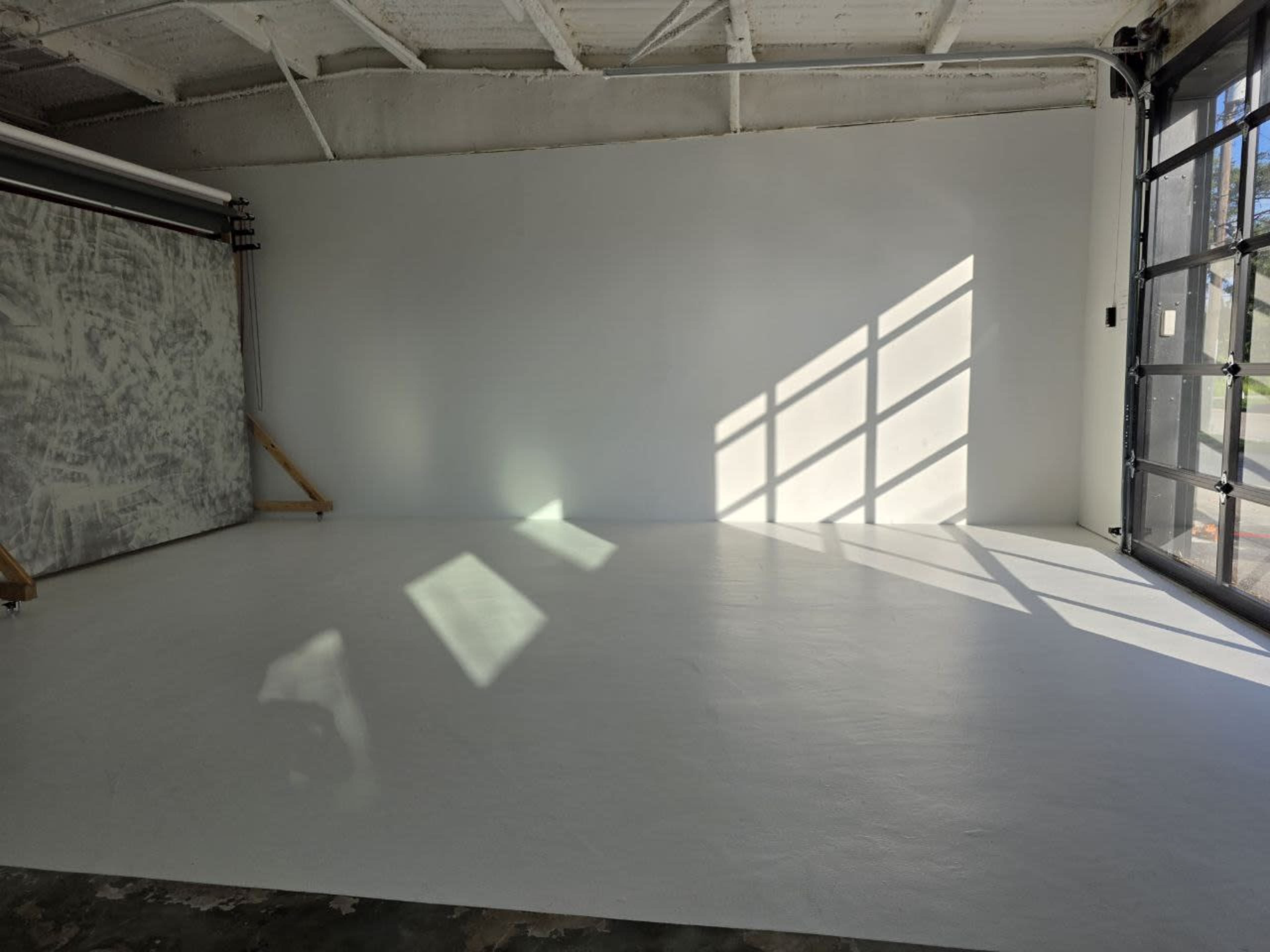 The image shows an empty studio space with a white floor and large windows casting shadows on the wall.