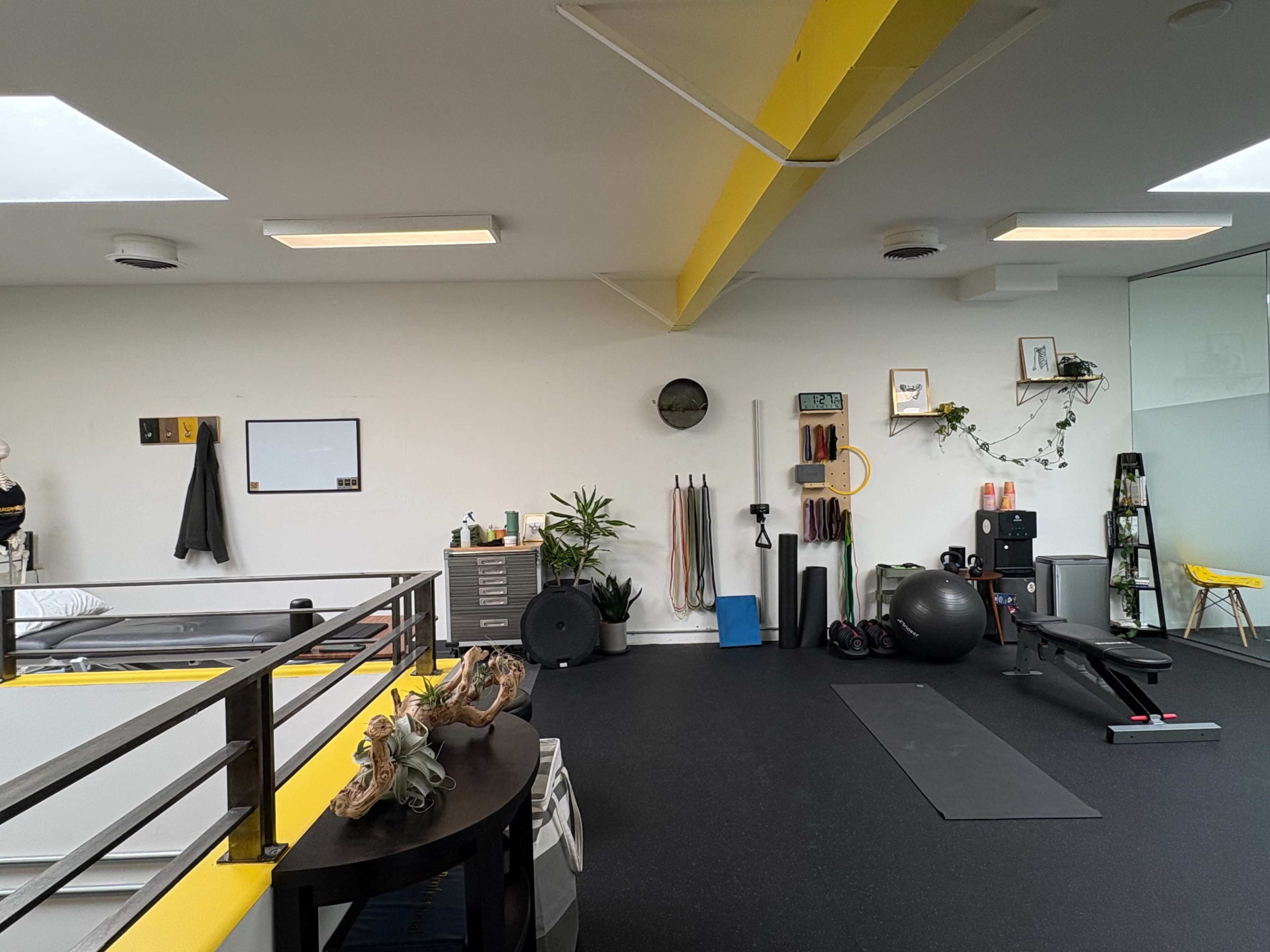 The image shows a minimalist fitness studio featuring exercise equipment, a rowing machine, and various fitness accessories arranged along the walls.