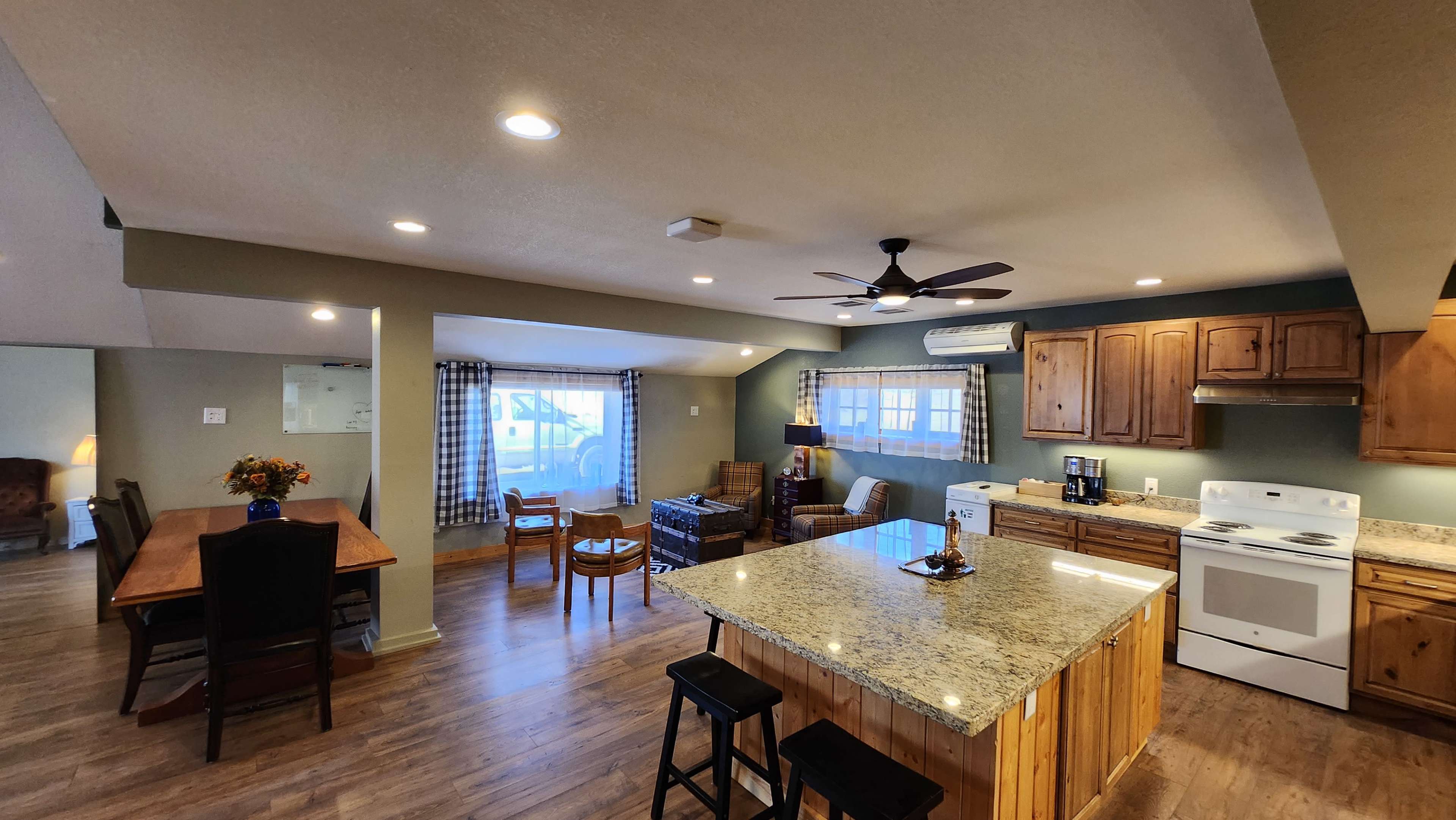 A spacious kitchen and dining area featuring wooden cabinets, a granite countertop island, and a seating arrangement with a dining table and chairs.
