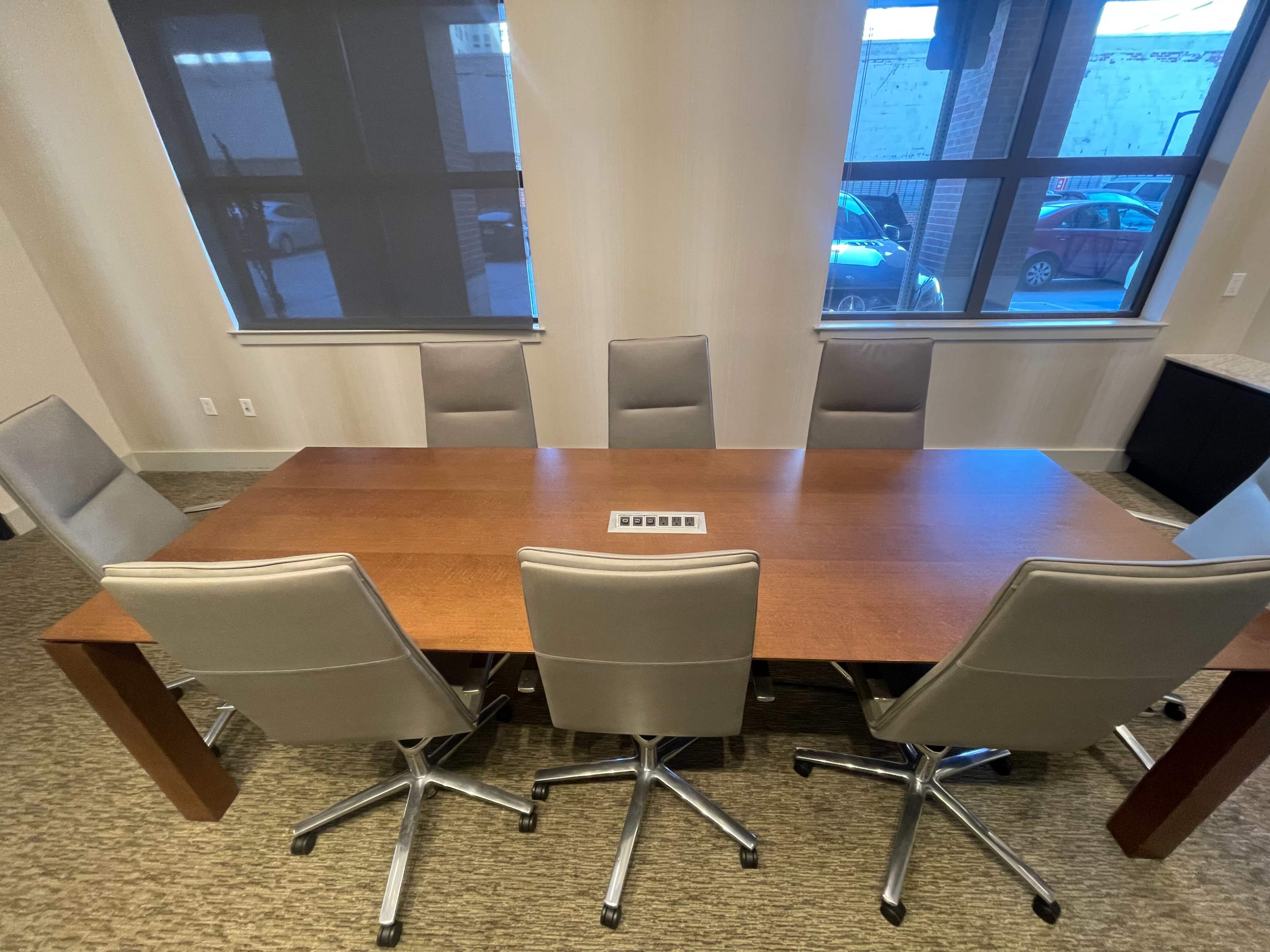 A large wooden conference table is surrounded by eight modern swivel chairs in a well-lit meeting room.