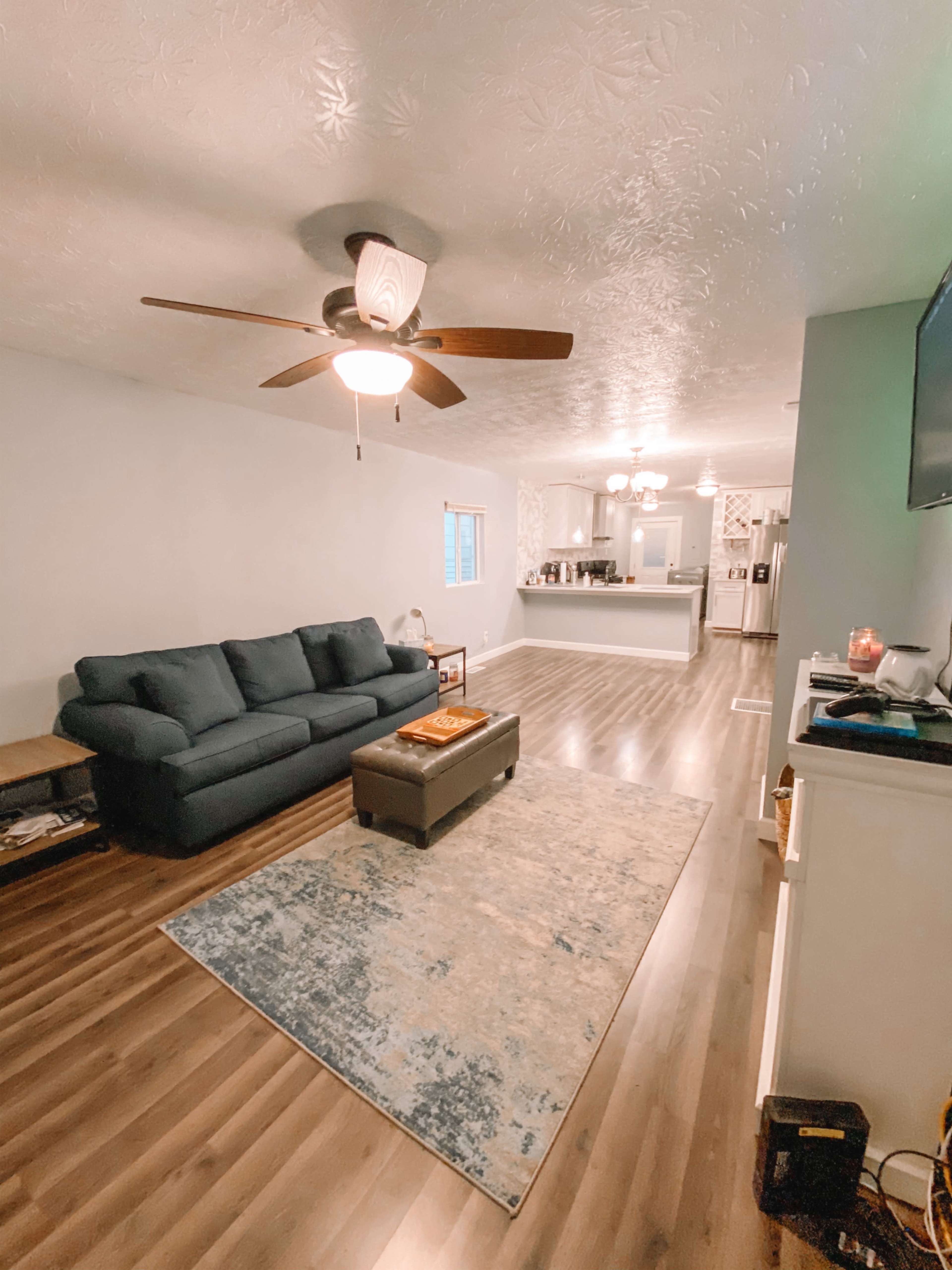 A spacious living room with a blue sofa, wooden flooring, and an open layout leading to a kitchen in the background.