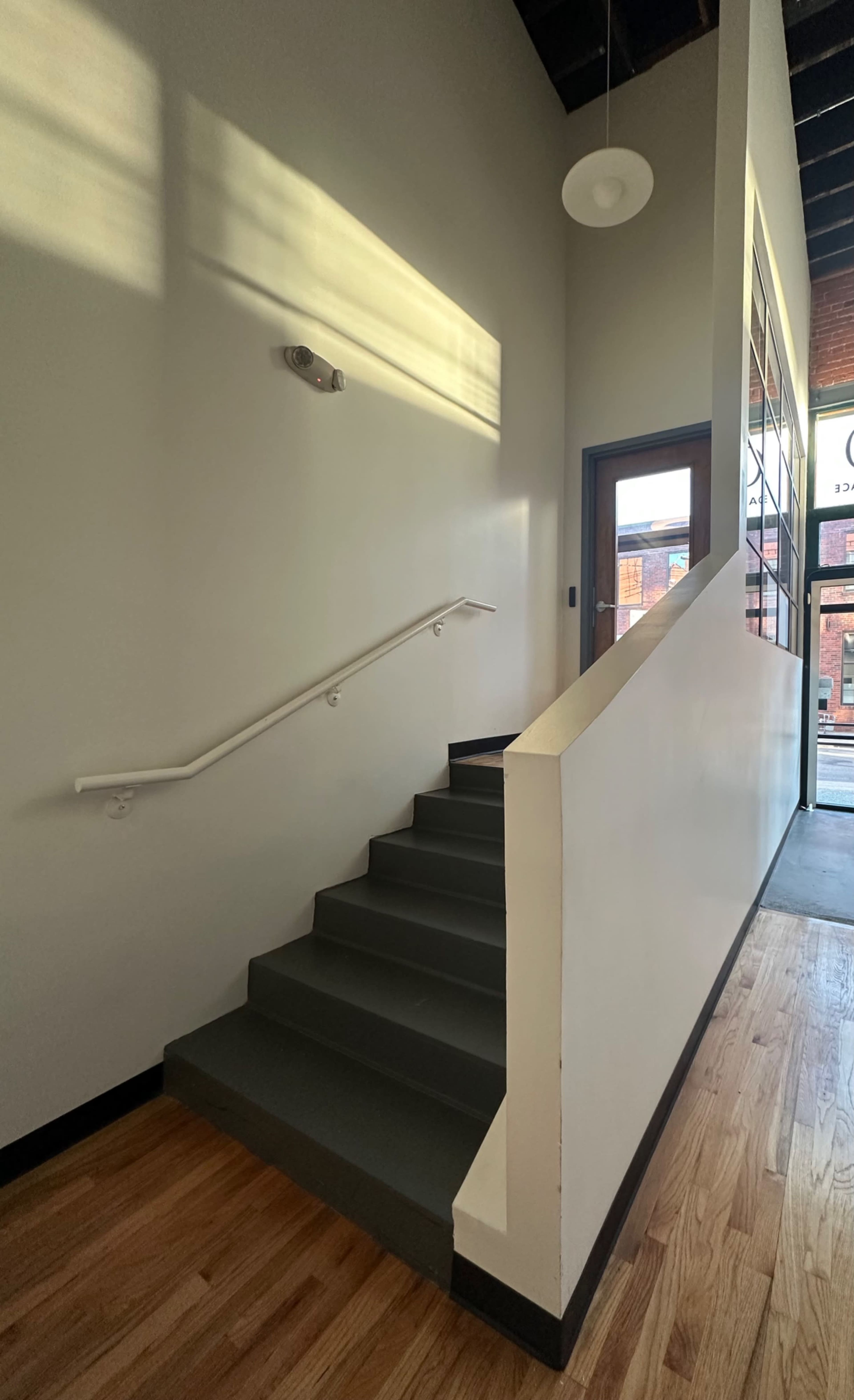 The image shows a staircase leading upward in a well-lit hallway with wooden floors and a contemporary design.