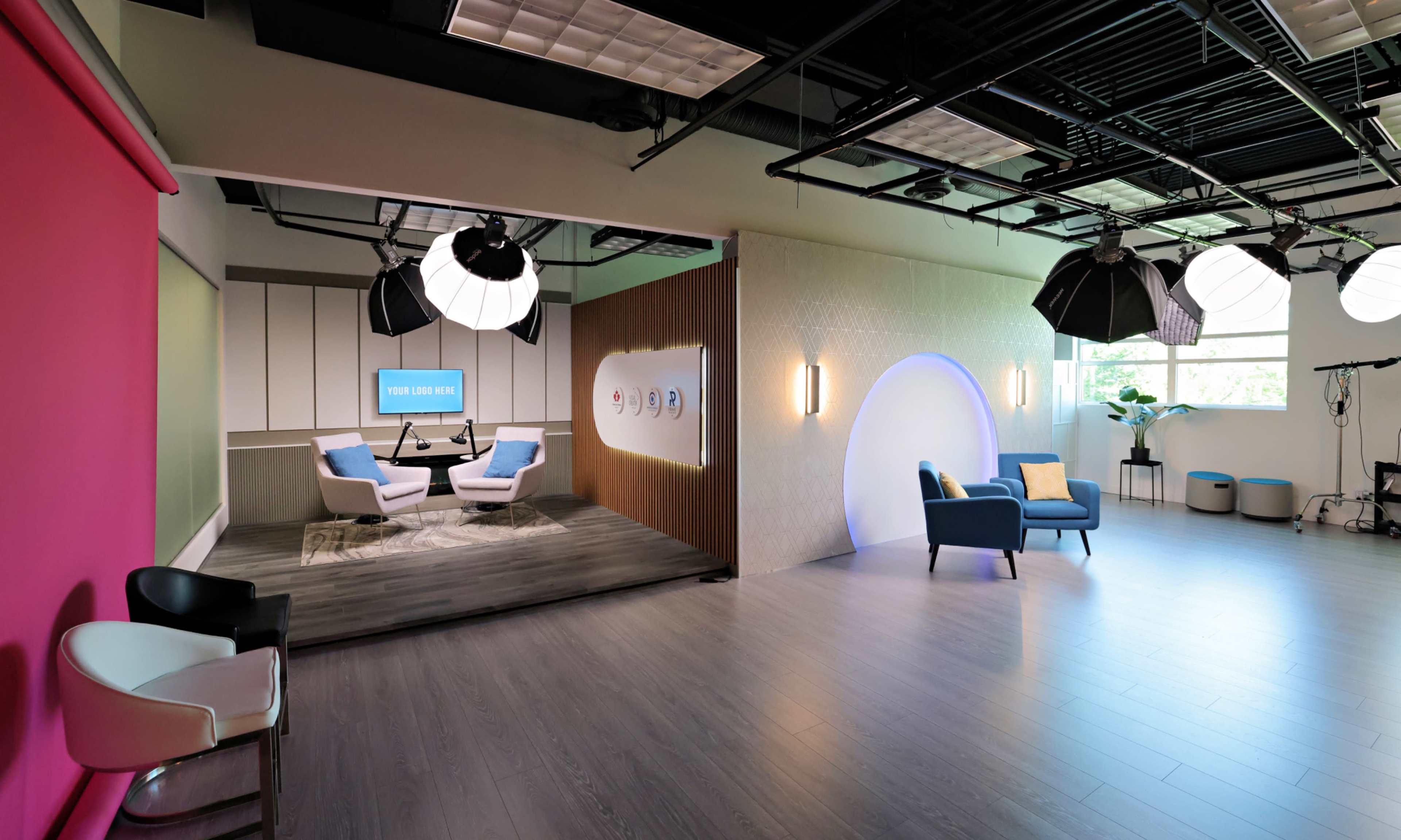 The image shows a modern studio space featuring distinct areas with colorful walls, comfortable seating, and professional lighting equipment.