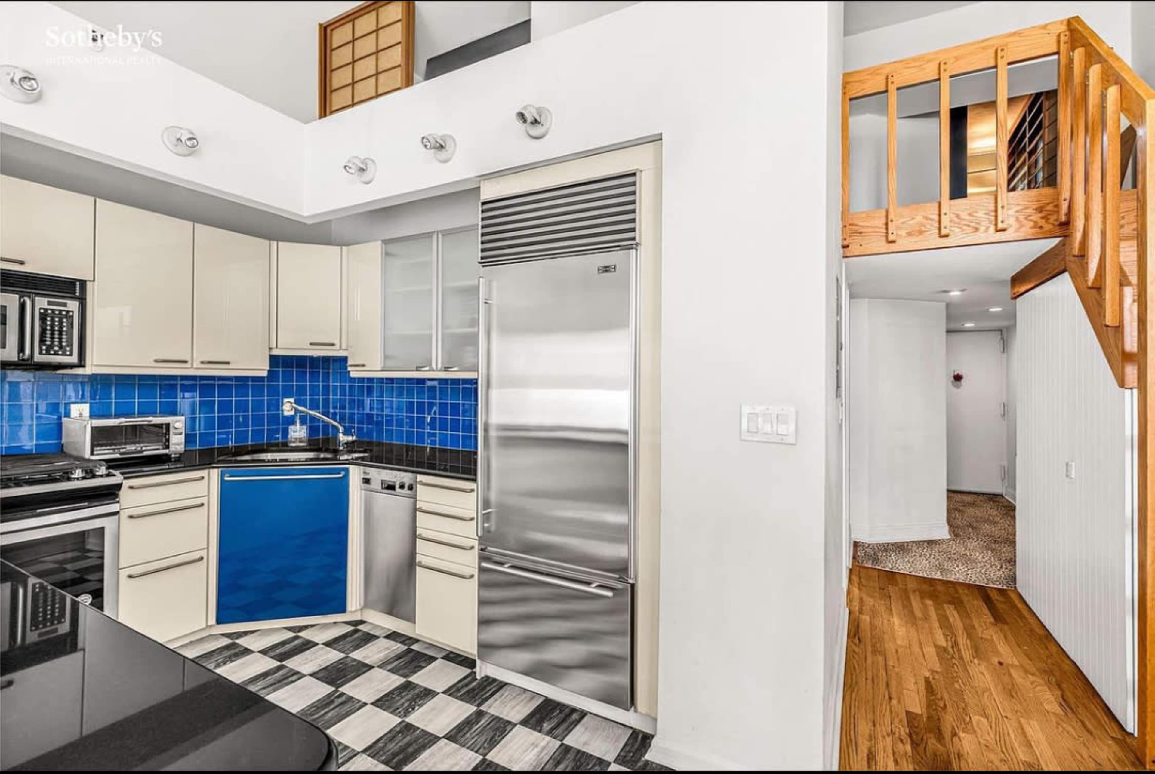 The image showcases a modern kitchen with stainless steel appliances, blue backsplash tiles, and an adjacent wooden staircase leading to a loft-like space.