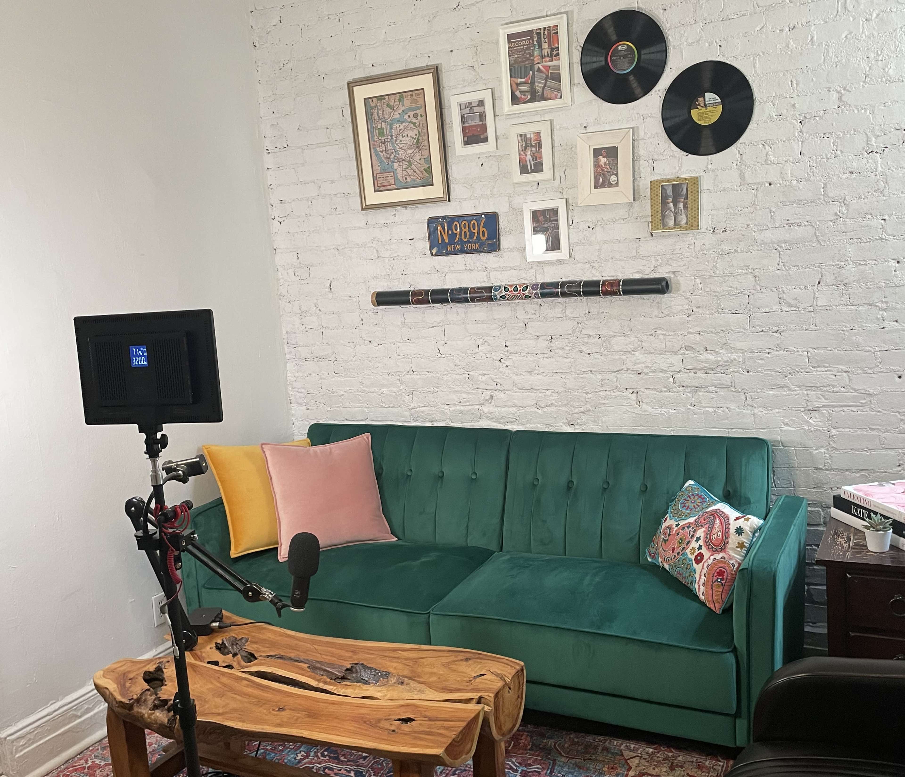 A teal couch with colorful pillows in a room featuring a white brick wall adorned with framed art and vinyl records.