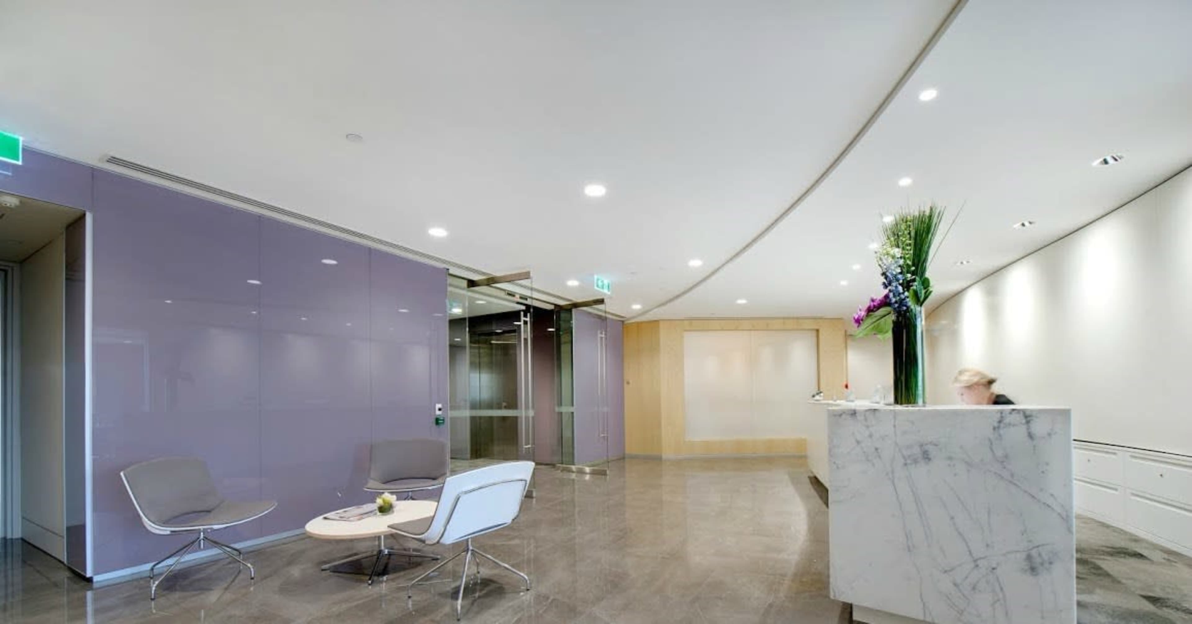 A modern reception area with a marble front desk, gray chairs, and a decorative floral arrangement in a minimalist design.