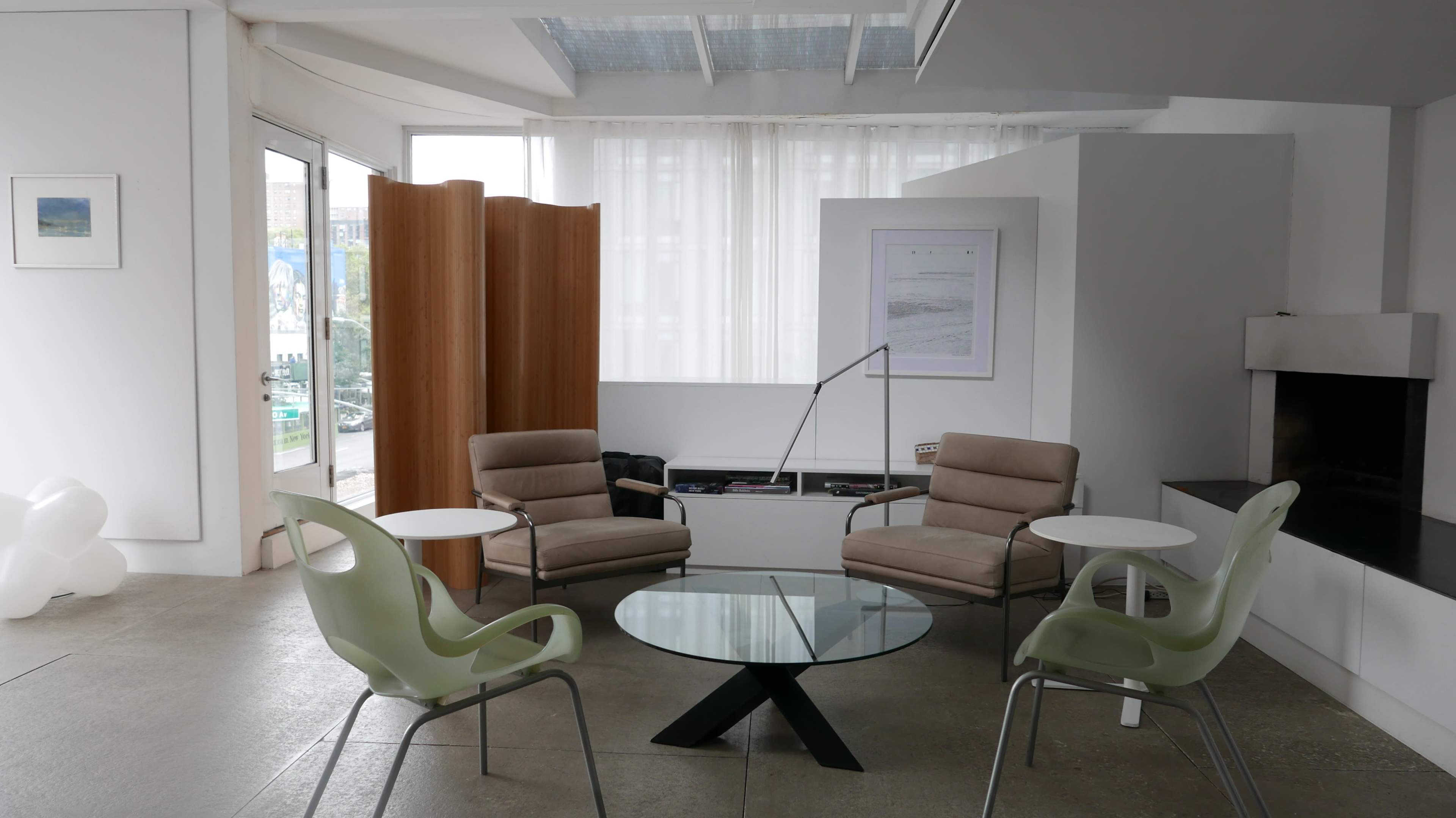 A modern interior space featuring a glass table surrounded by four chairs, with a partition and large windows letting in natural light.