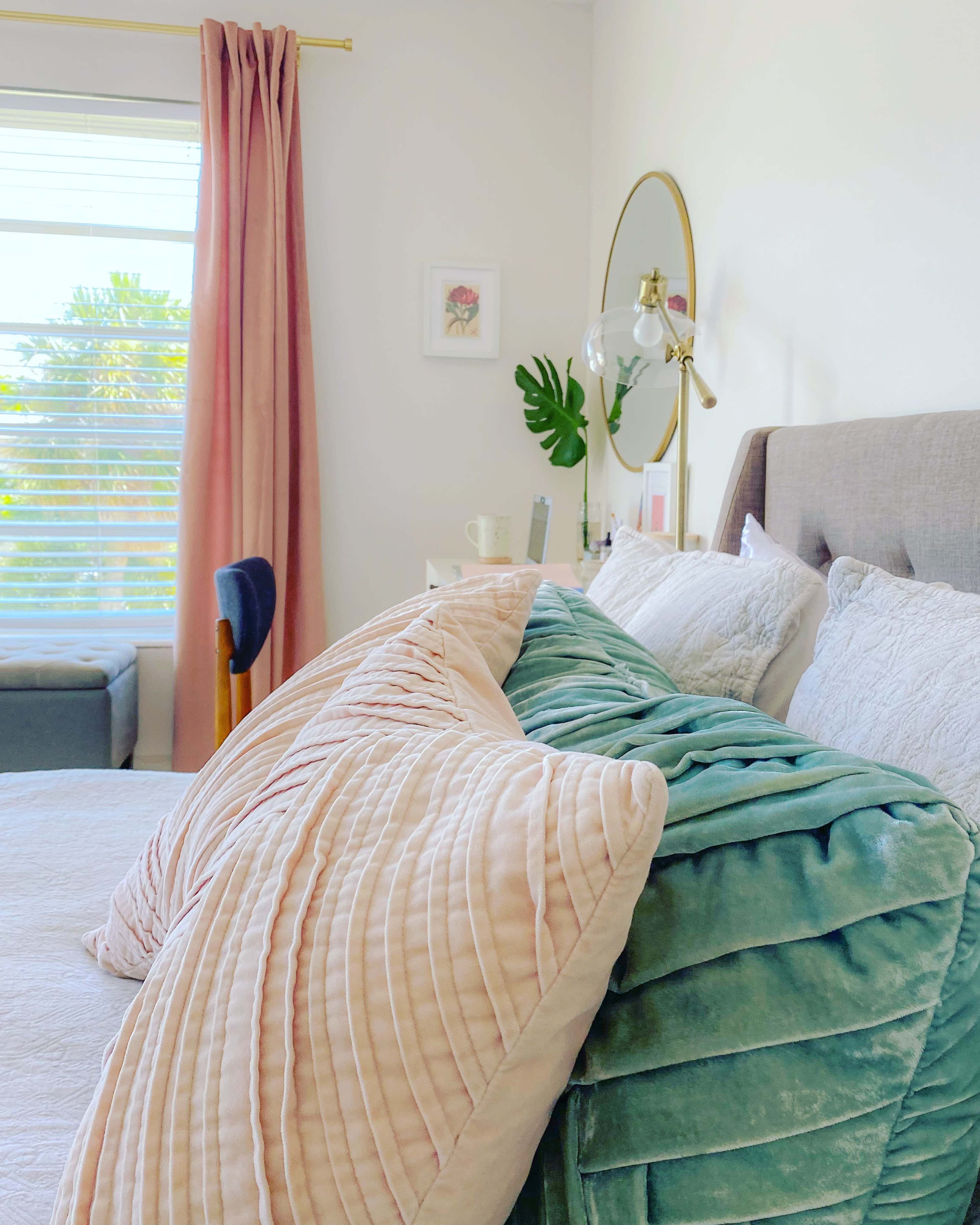A neatly arranged bedroom with a bed adorned with cushions, a lamp beside it, and a window framed by pink curtains.