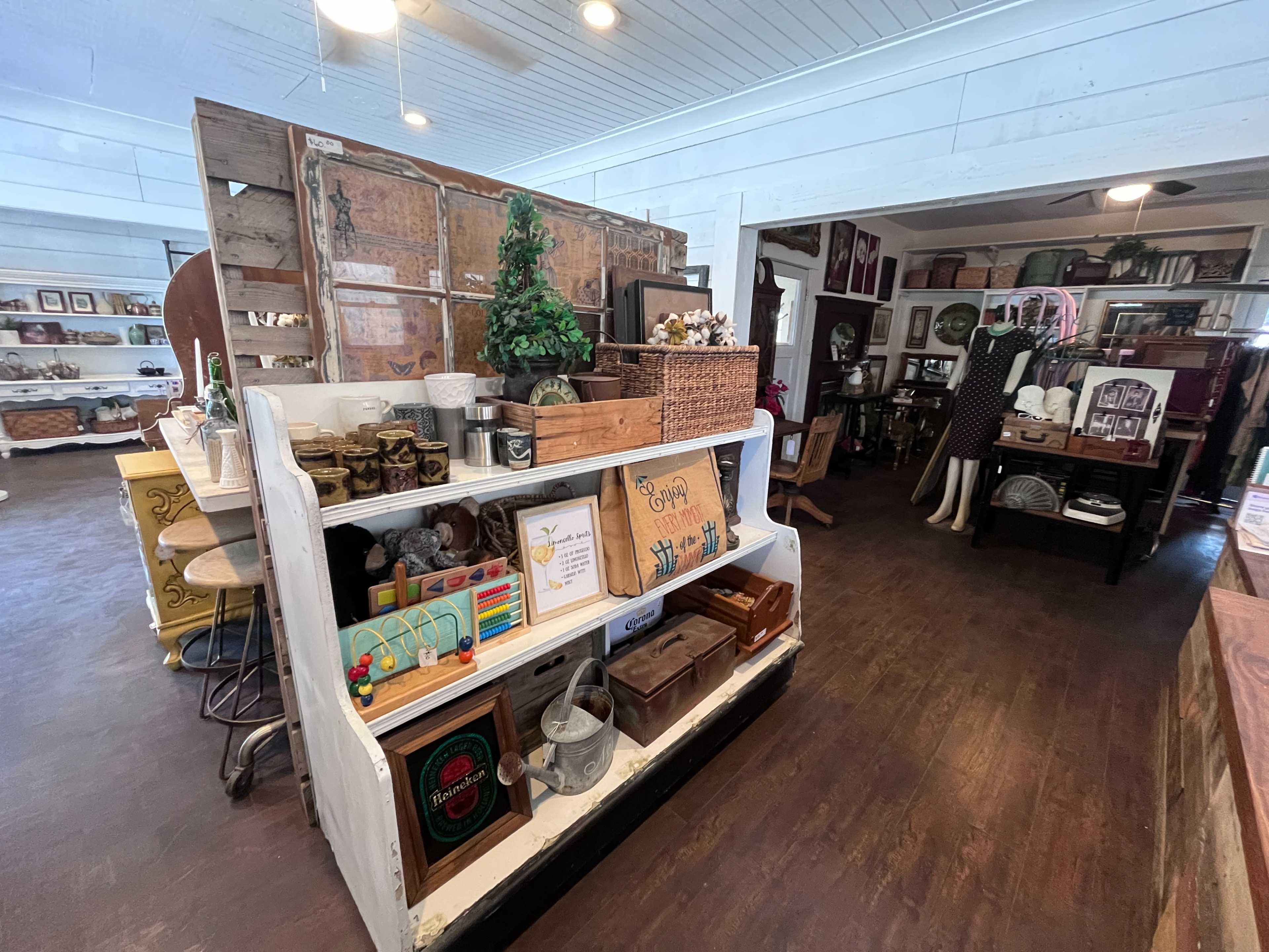 The image shows a shop interior filled with various vintage and decorative items displayed on shelves and tables.