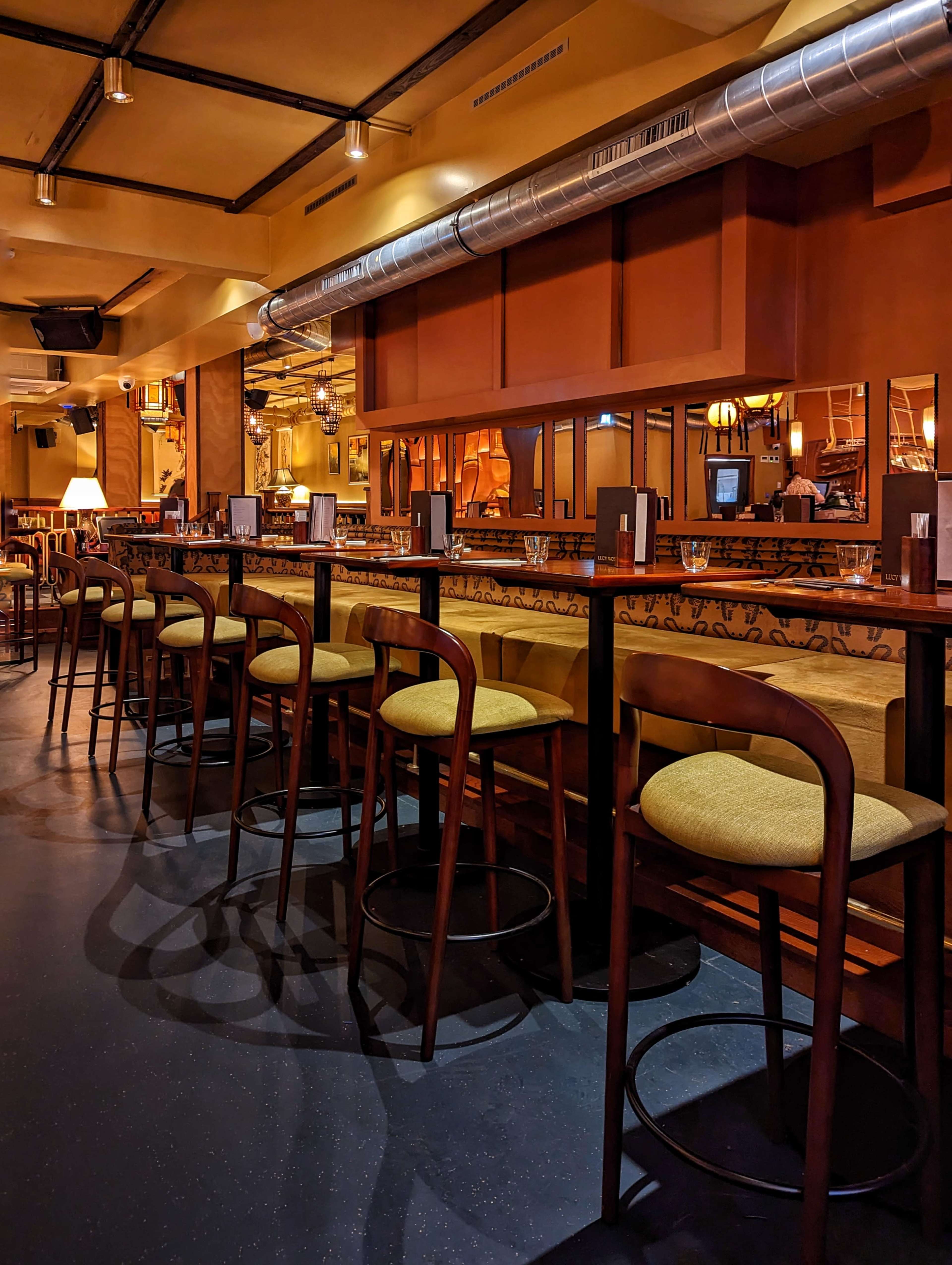 The image shows a restaurant interior with a long bar counter lined with high stools and warm, dim lighting.