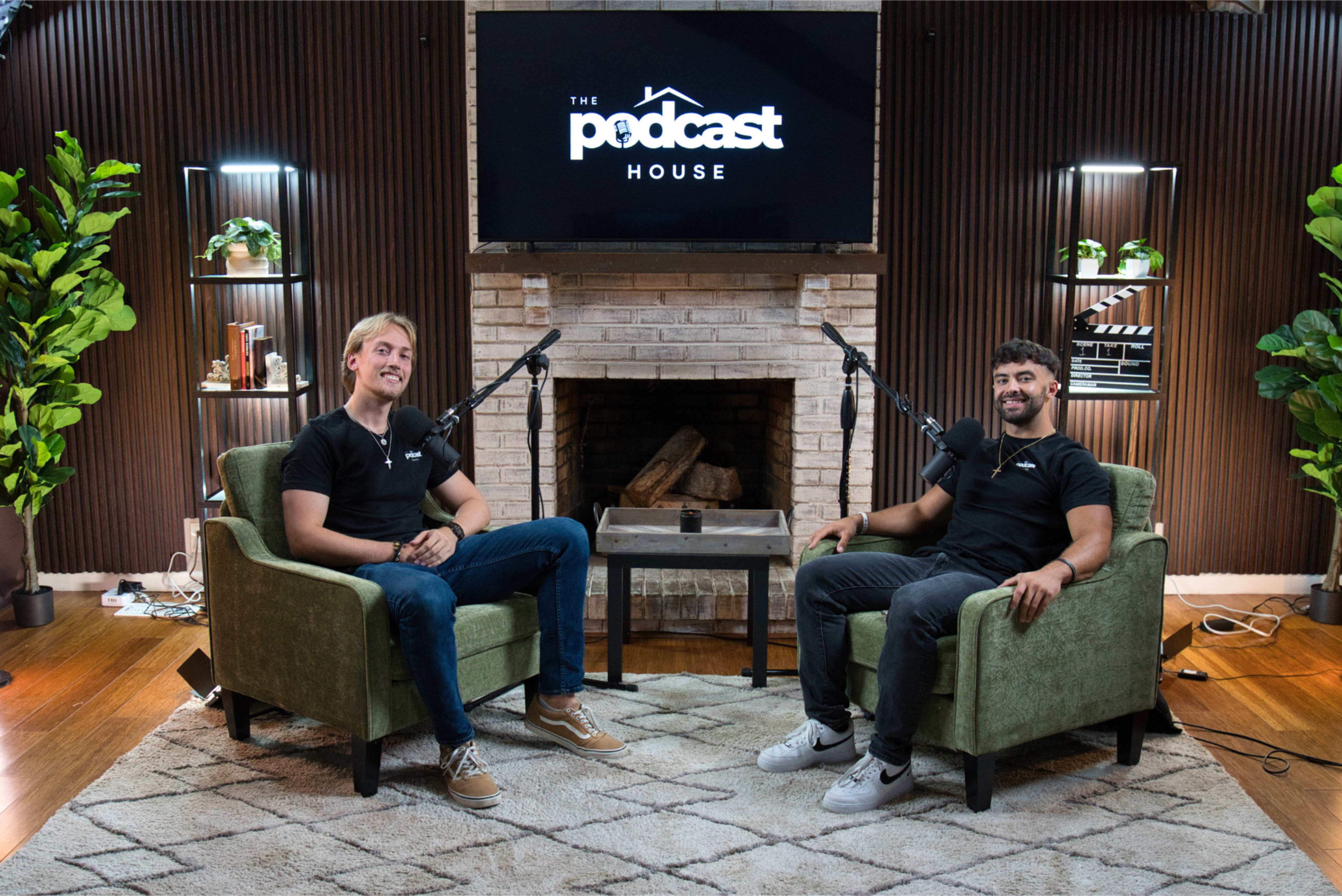 Two individuals sit in green chairs facing each other in a podcast studio, with microphones in front of them and a large screen displaying "The Podcast House" in the background.