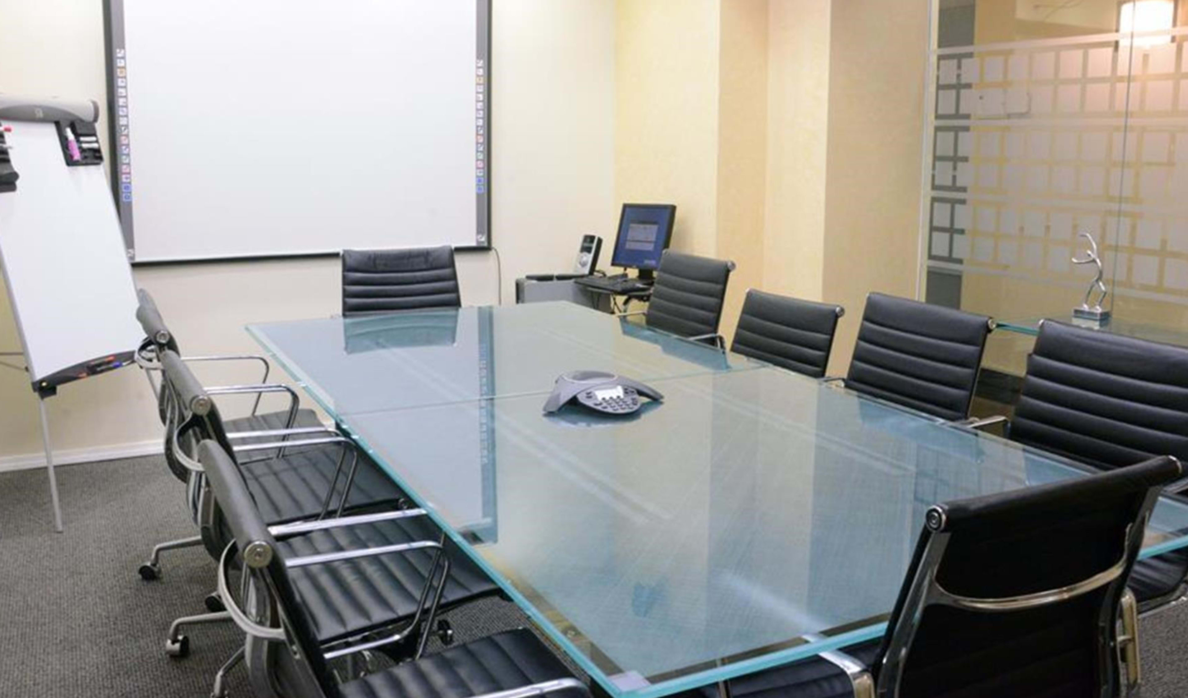 A modern conference room features a glass table surrounded by black chairs, with a whiteboard and a computer in the background.