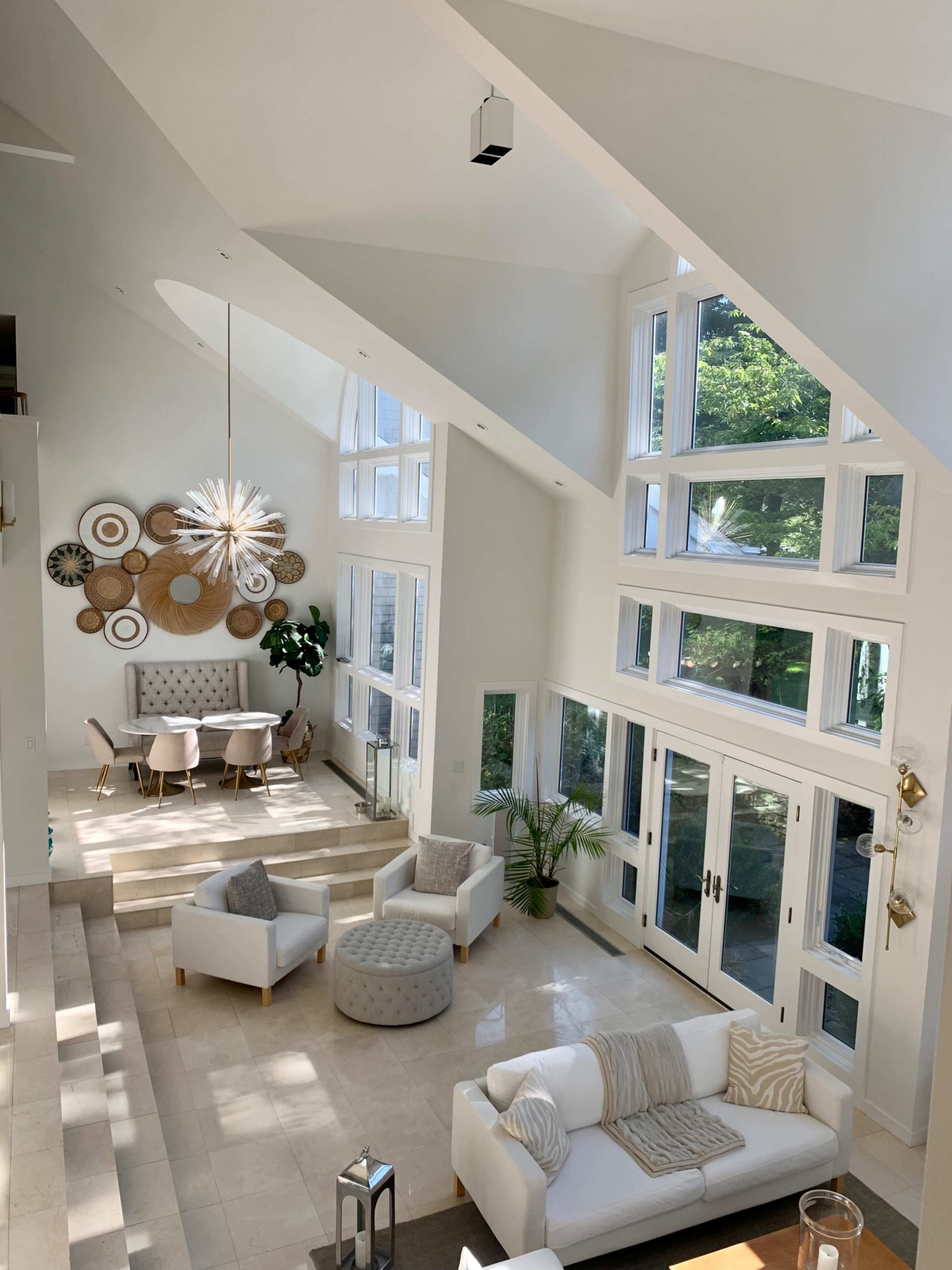 A bright, modern living room featuring a large window wall, stylish furniture, and a dining area near a sunny corner.