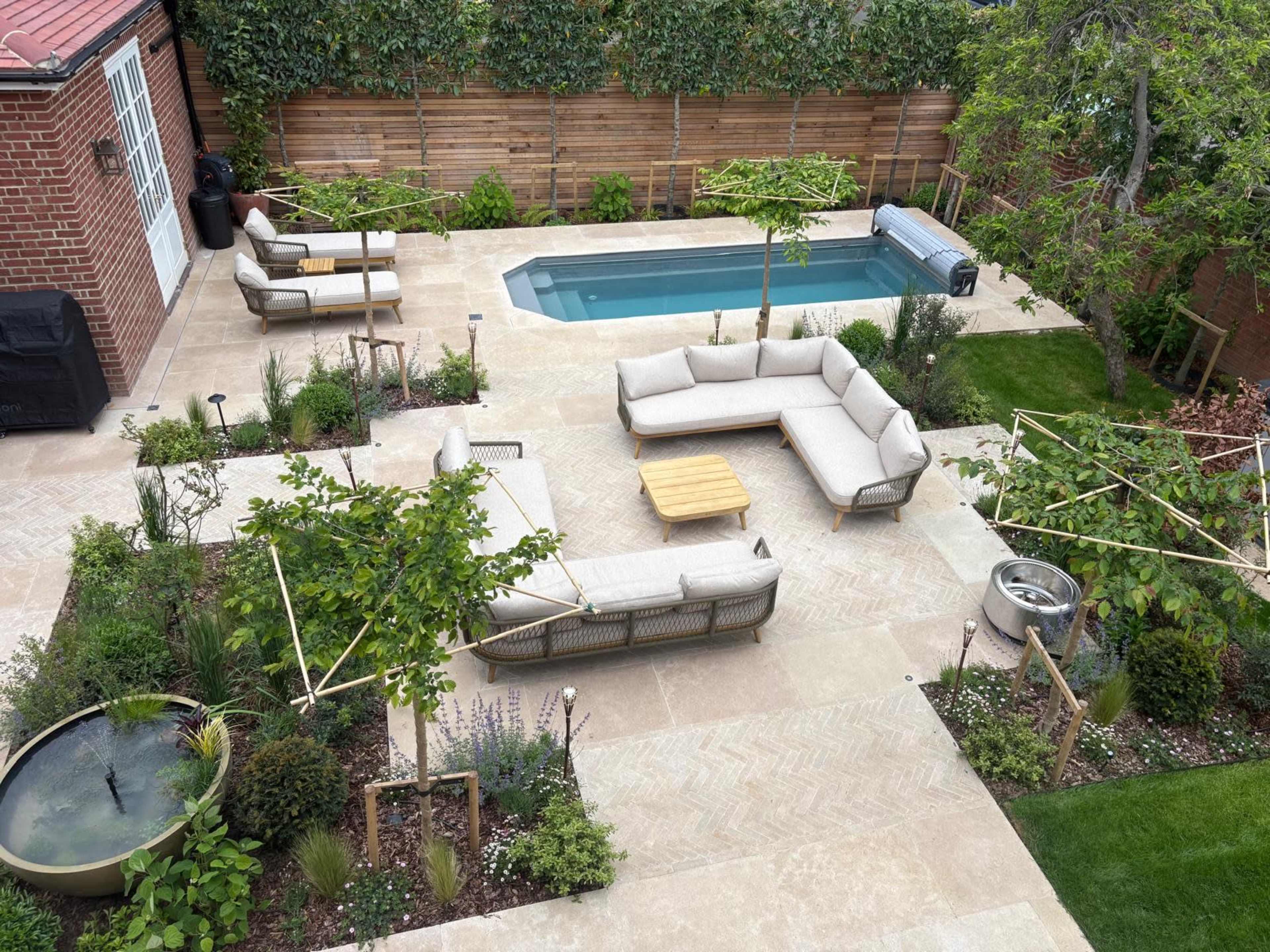 The image shows a landscaped backyard featuring a swimming pool, multiple seating areas with outdoor furniture, and a variety of plants and trees.