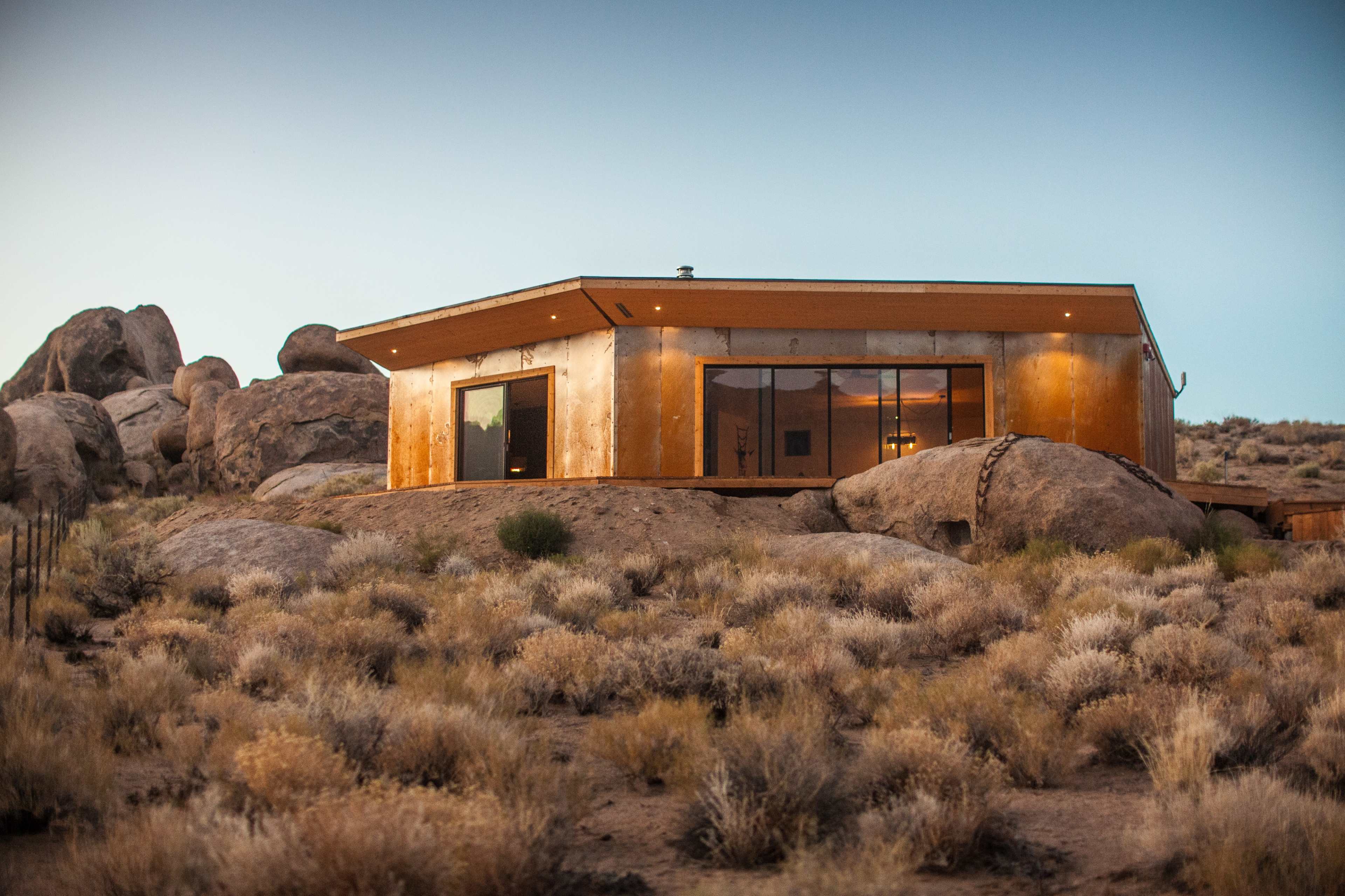 A modern house with large windows is situated among rocky terrain and sparse vegetation.