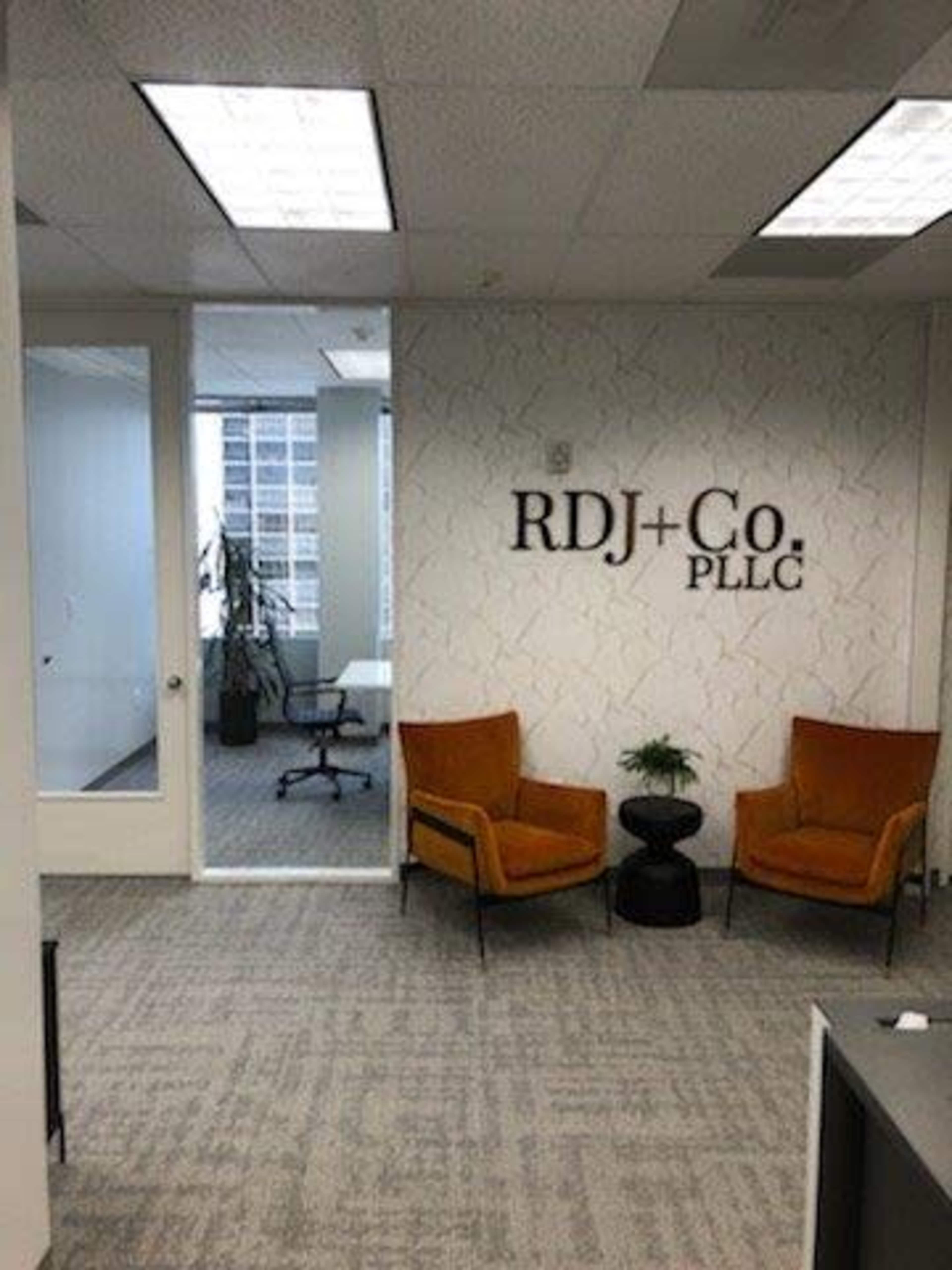 A modern office space with two orange chairs, a small black table, and a sign for "RDJ+Co. PLLC" on the textured wall.
