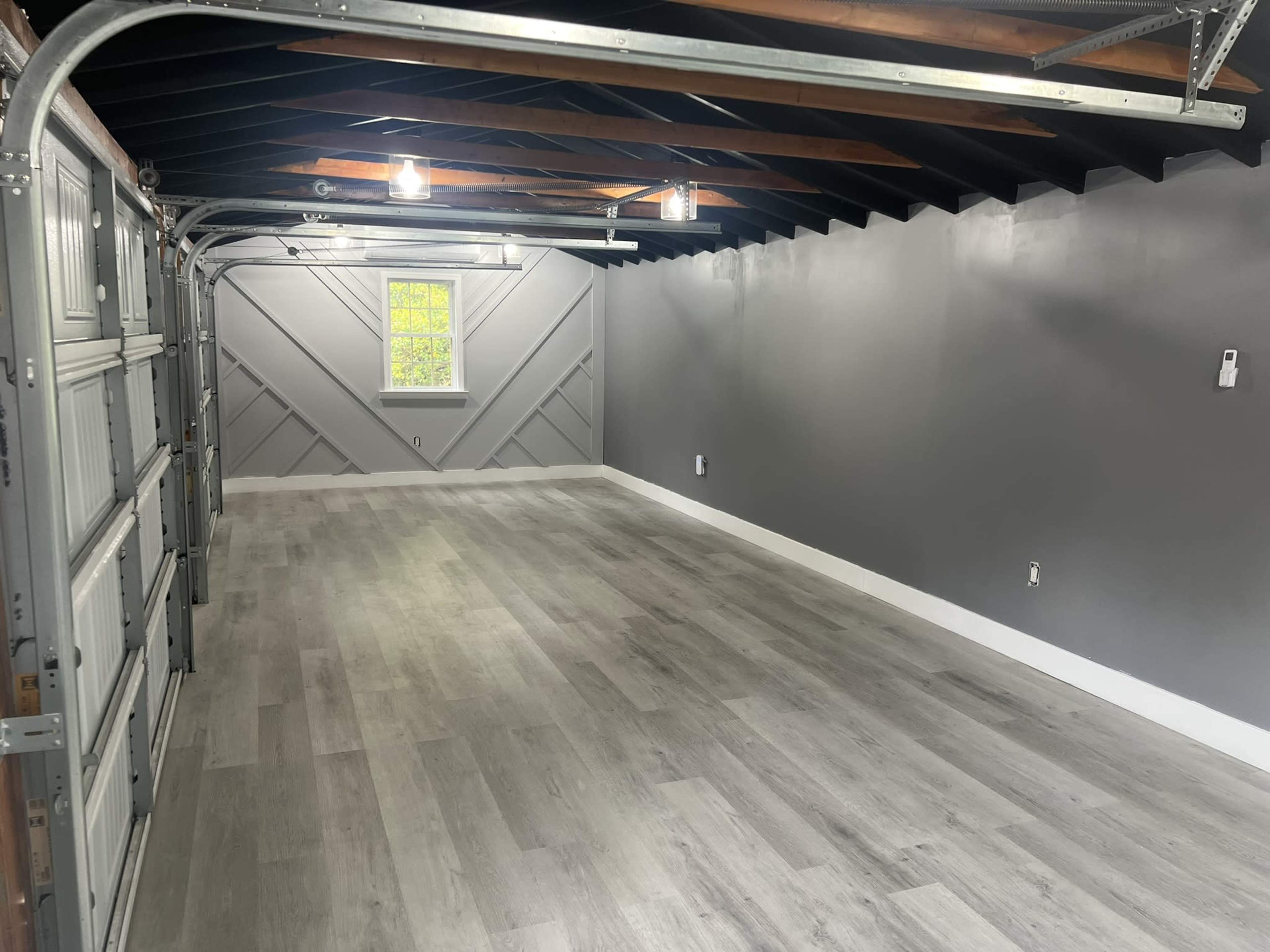 A clean, empty garage with light gray walls, a window, and a polished wood floor.