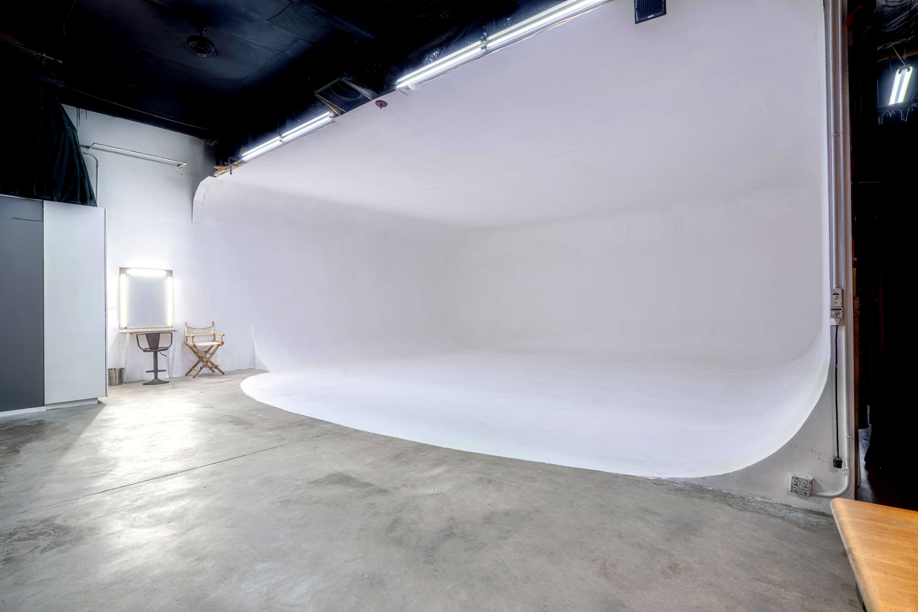 A minimalist photography studio with a seamless white backdrop and concrete flooring.