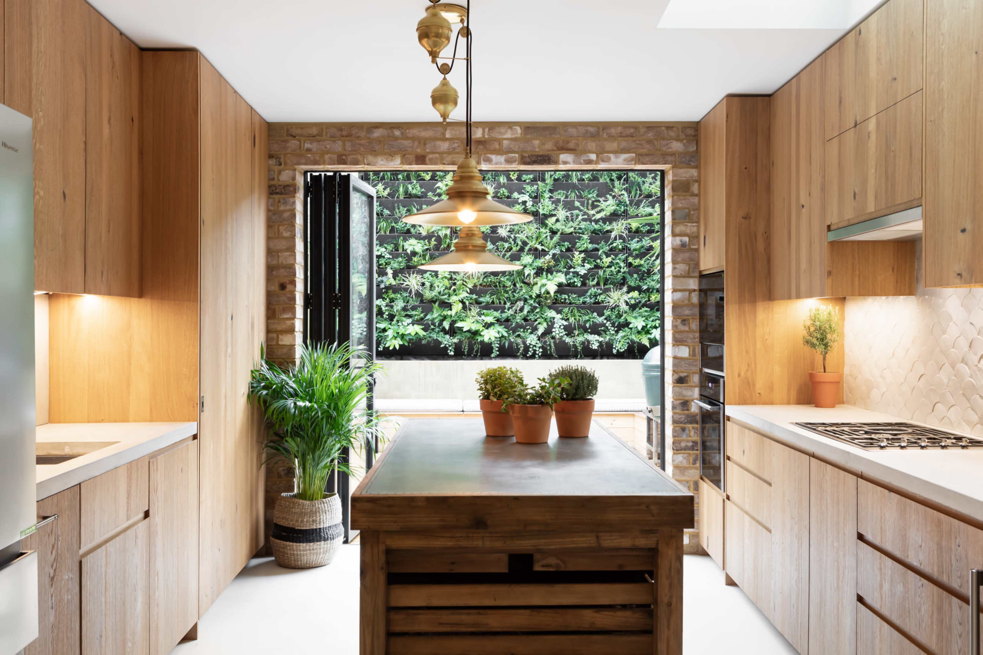 A modern kitchen features wooden cabinetry, a central island, and large windows overlooking a green outdoor space.