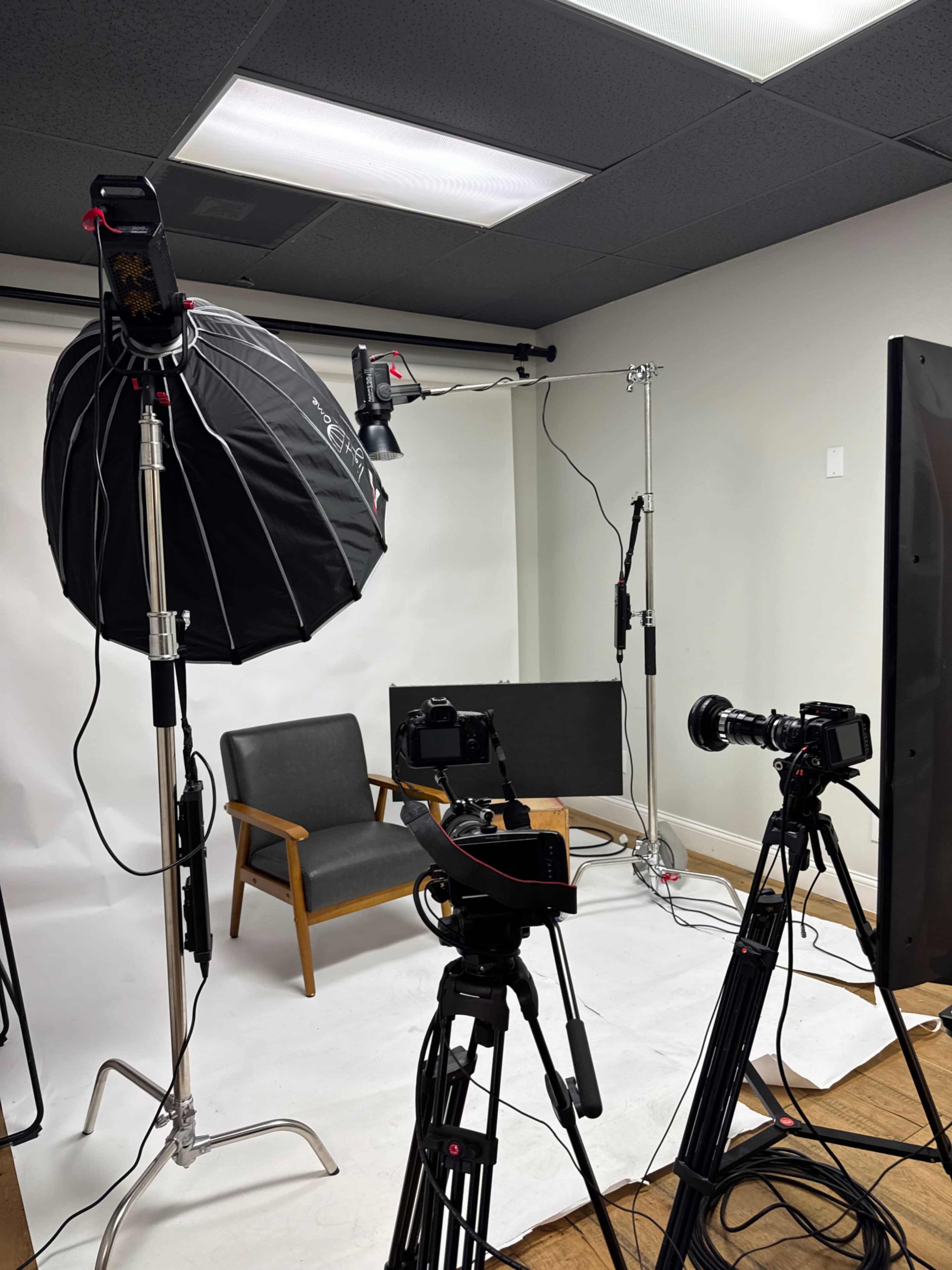 The image shows a photography studio setup with a chair, backdrop, lighting equipment, and multiple cameras positioned on tripods.