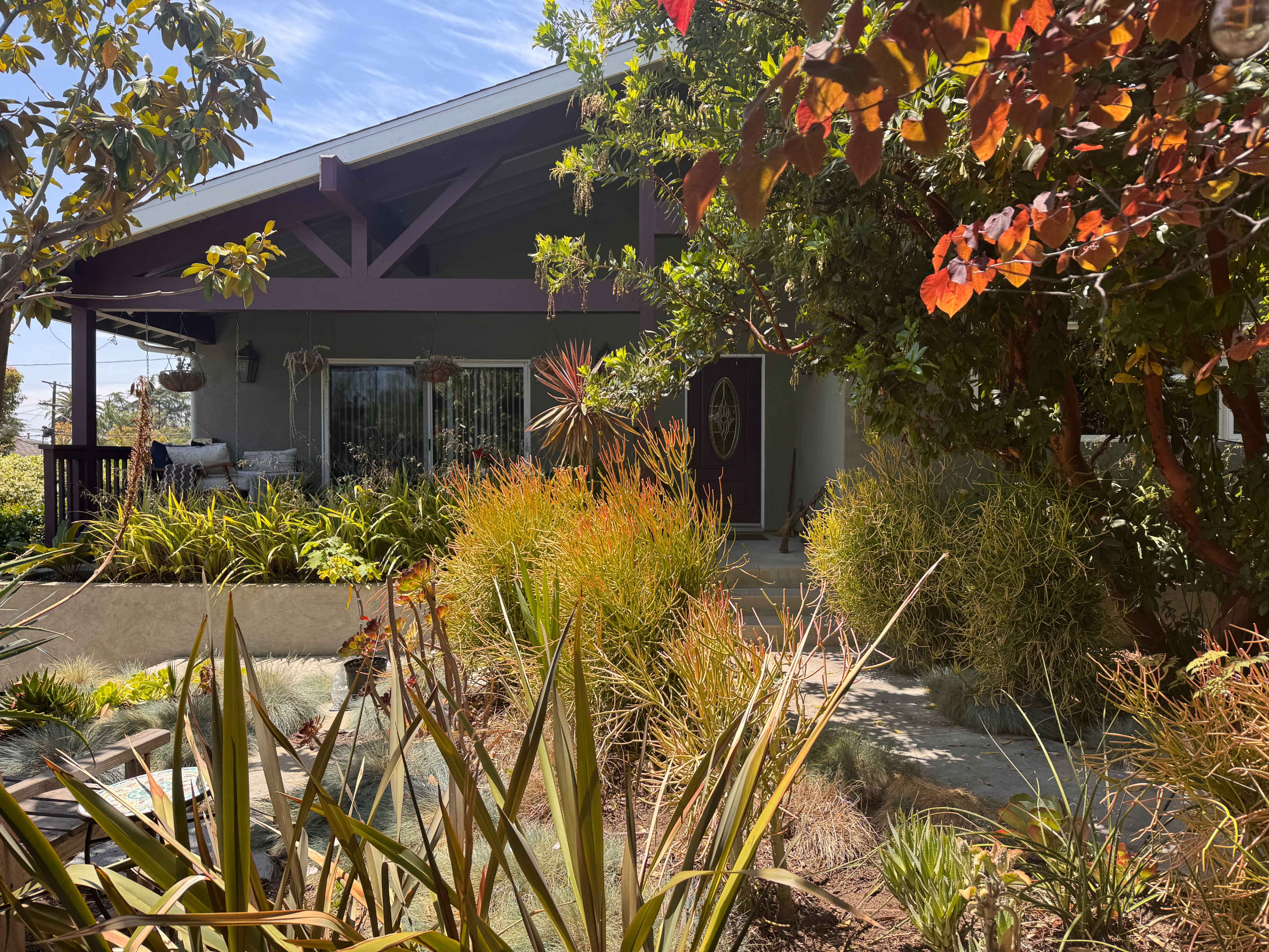 A well-maintained house with a porch is surrounded by various plants and colorful foliage.