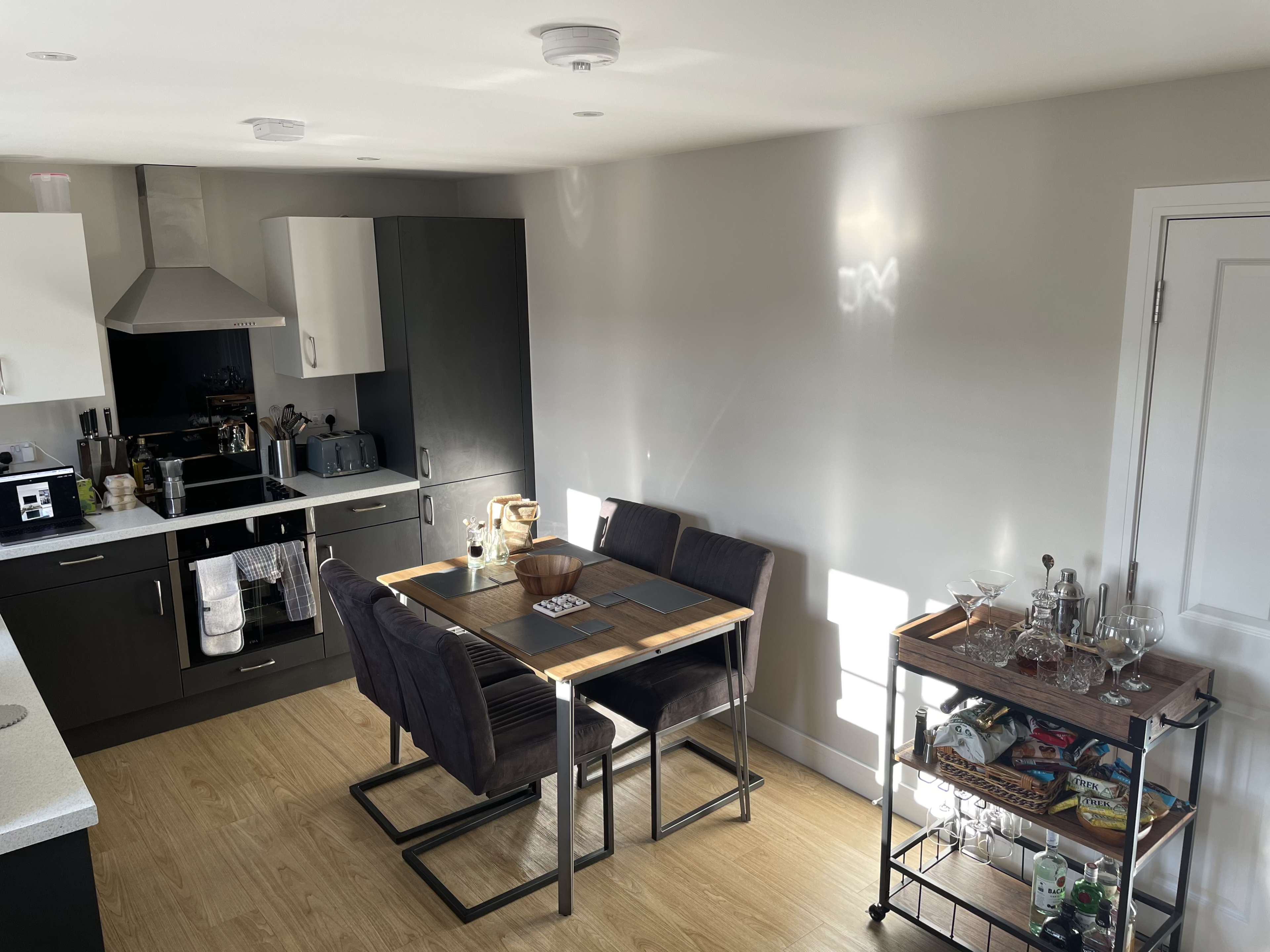 A modern kitchen includes a dining table with four chairs, a bar cart, and various kitchen appliances.