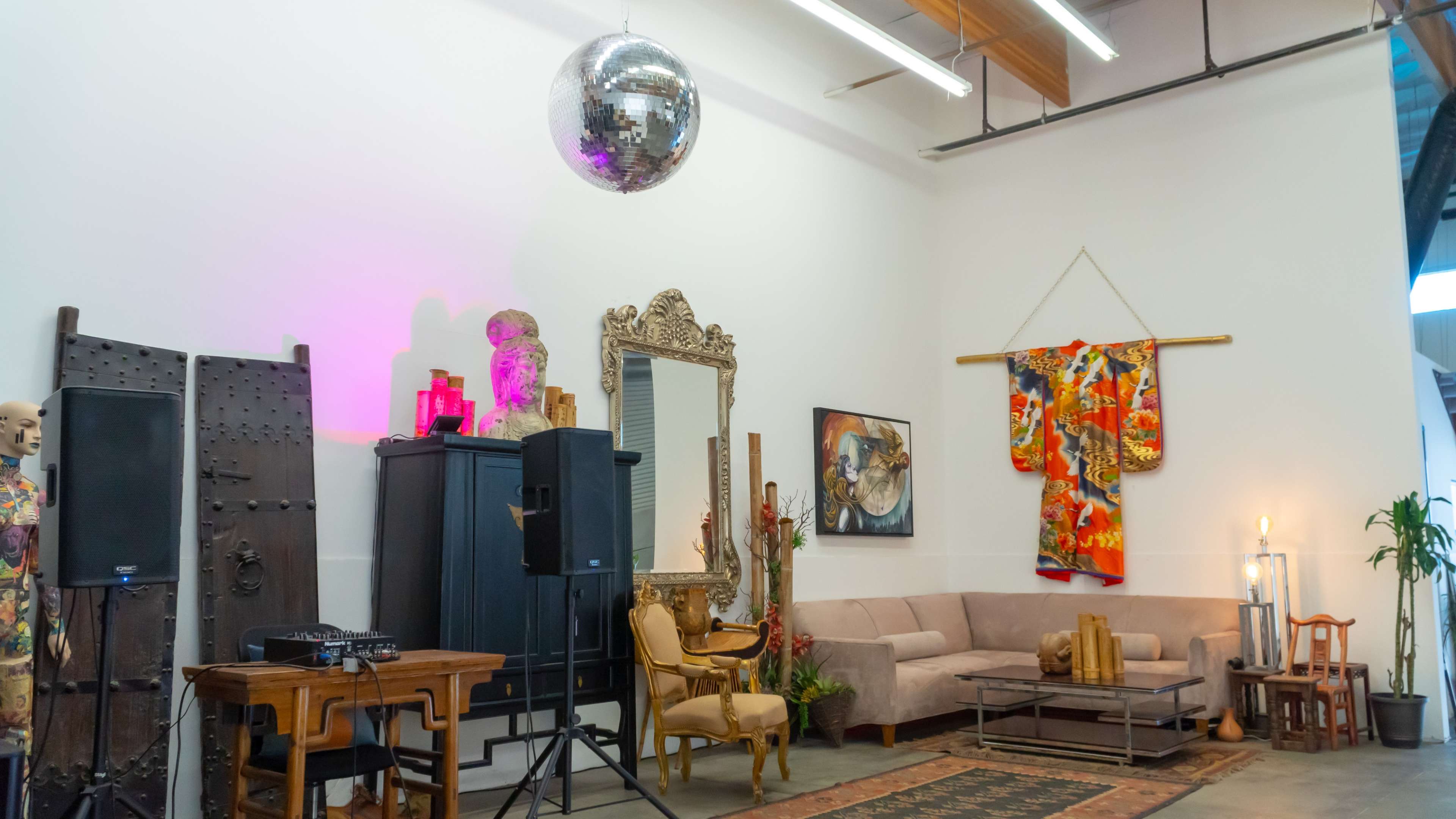 The image shows a spacious interior with a disco ball hanging from the ceiling, a wooden table and chairs, a large mirror, a colorful kimono displayed on the wall, and various decorative elements.