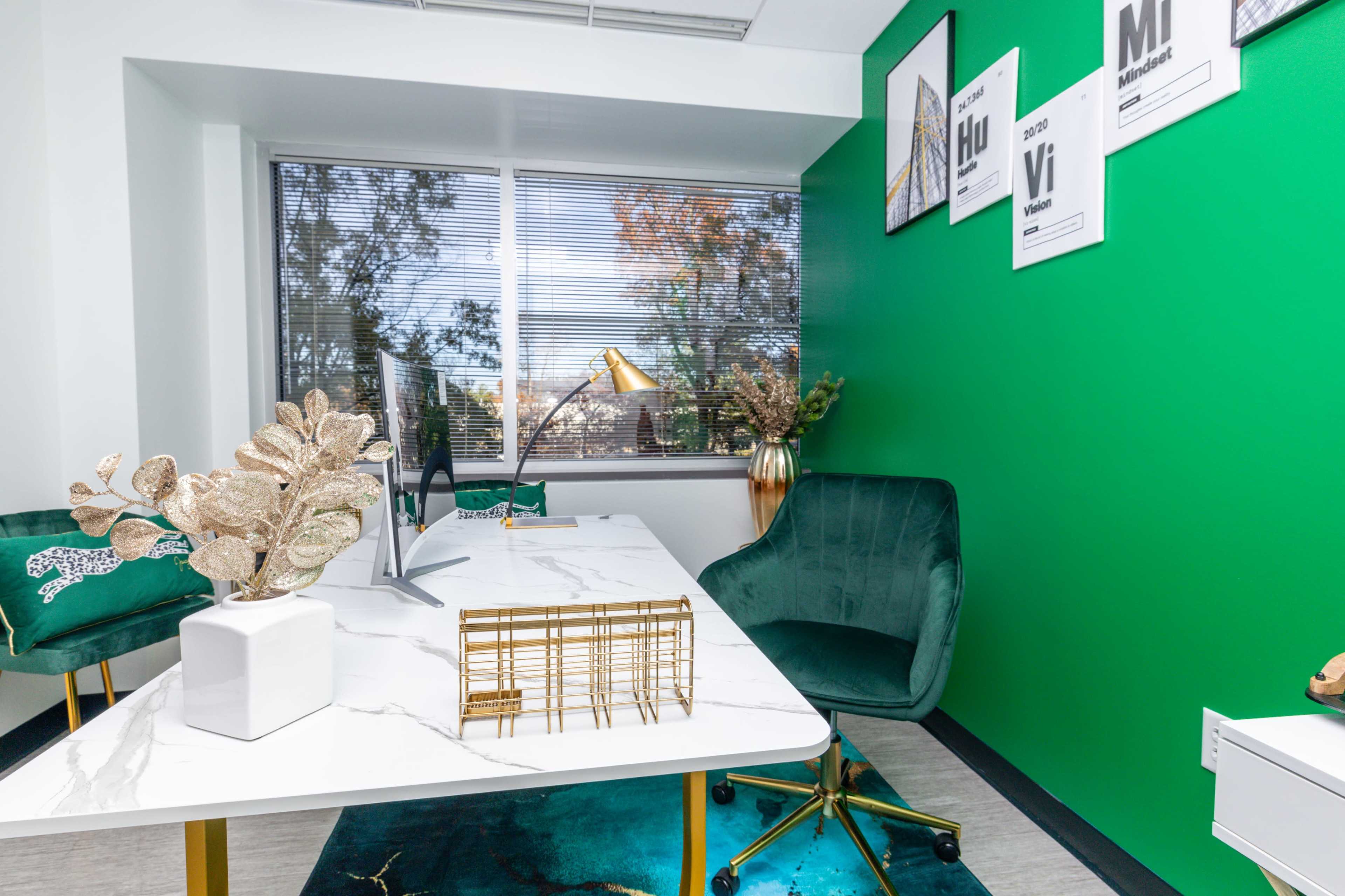 A neatly organized office space with a green accent wall, a white marble desk, a computer, and decorative plants.