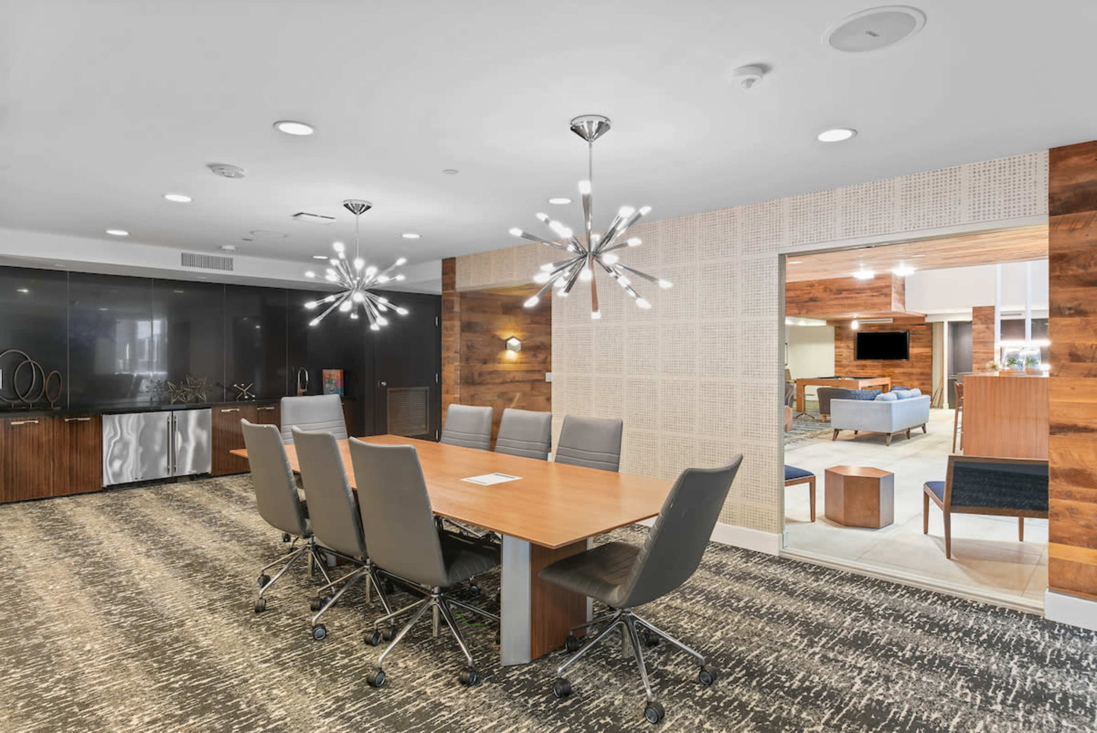 A modern conference room features a long wooden table surrounded by sleek chairs and illuminated by distinctive light fixtures.