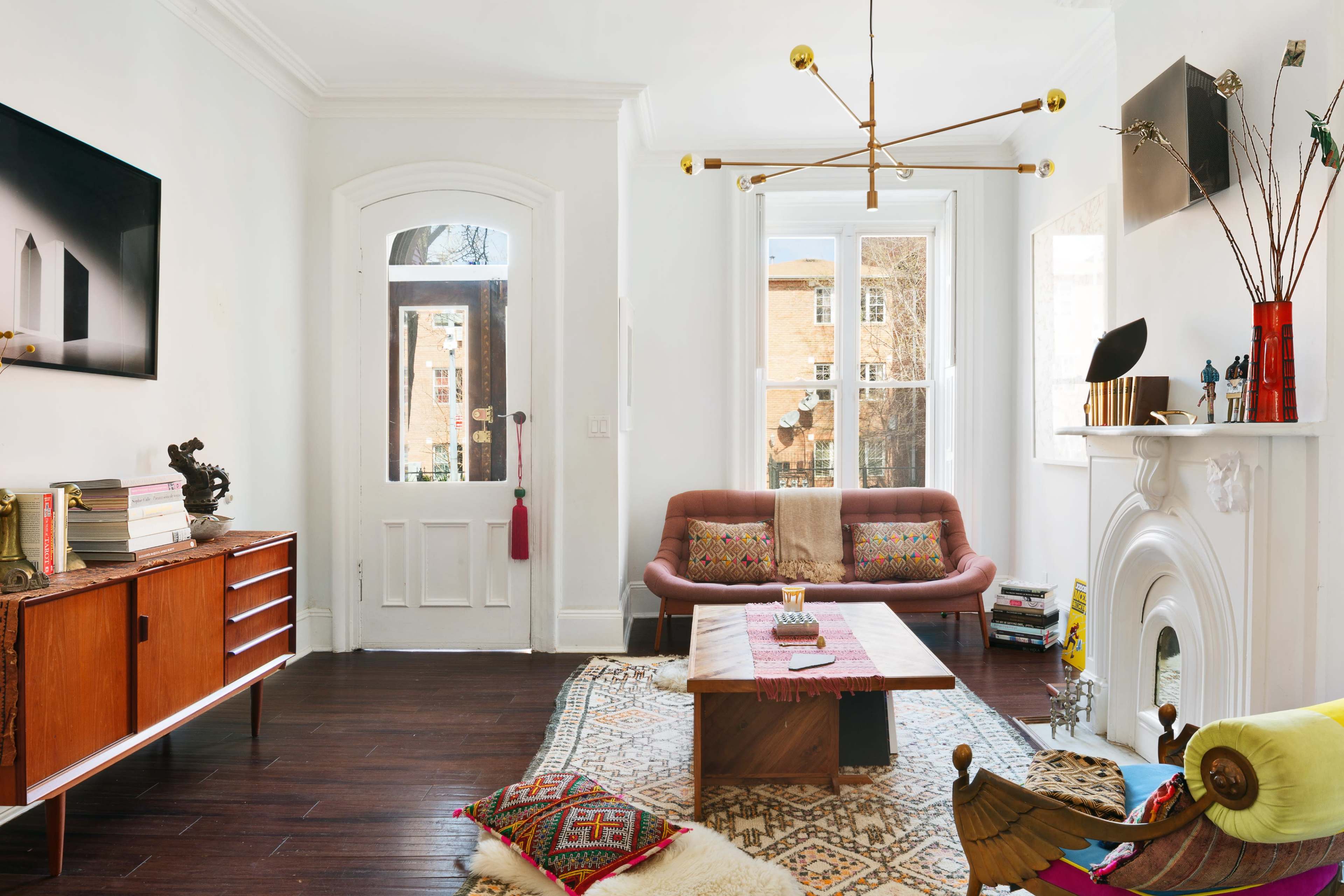 A well-lit living room featuring a modern sofa, a wooden coffee table, and decorative elements including a chandelier and various ornaments on a mantel.