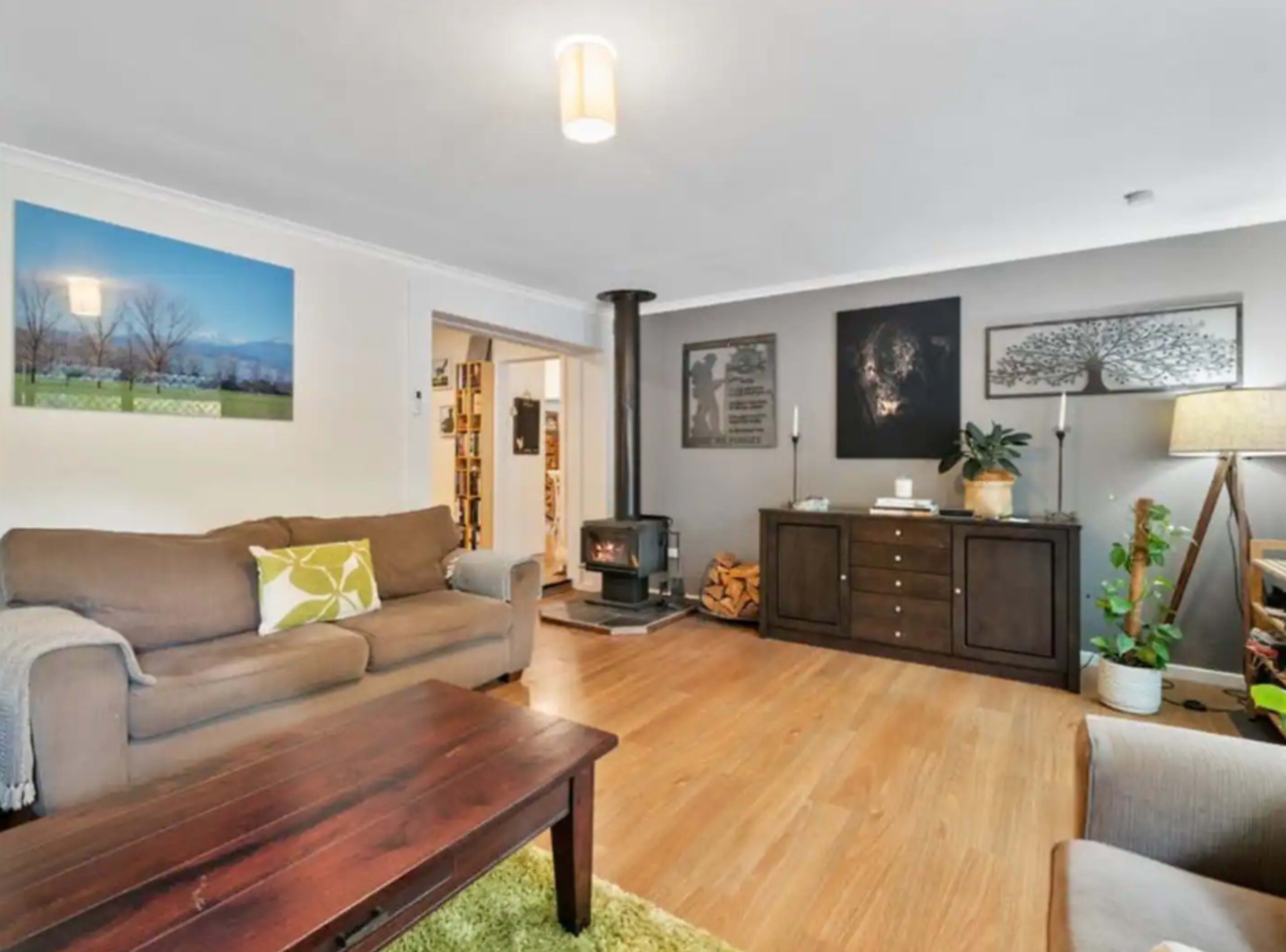 The living room features a brown sofa, a wooden coffee table, a wood stove, and various wall decorations, including artwork and a plant.