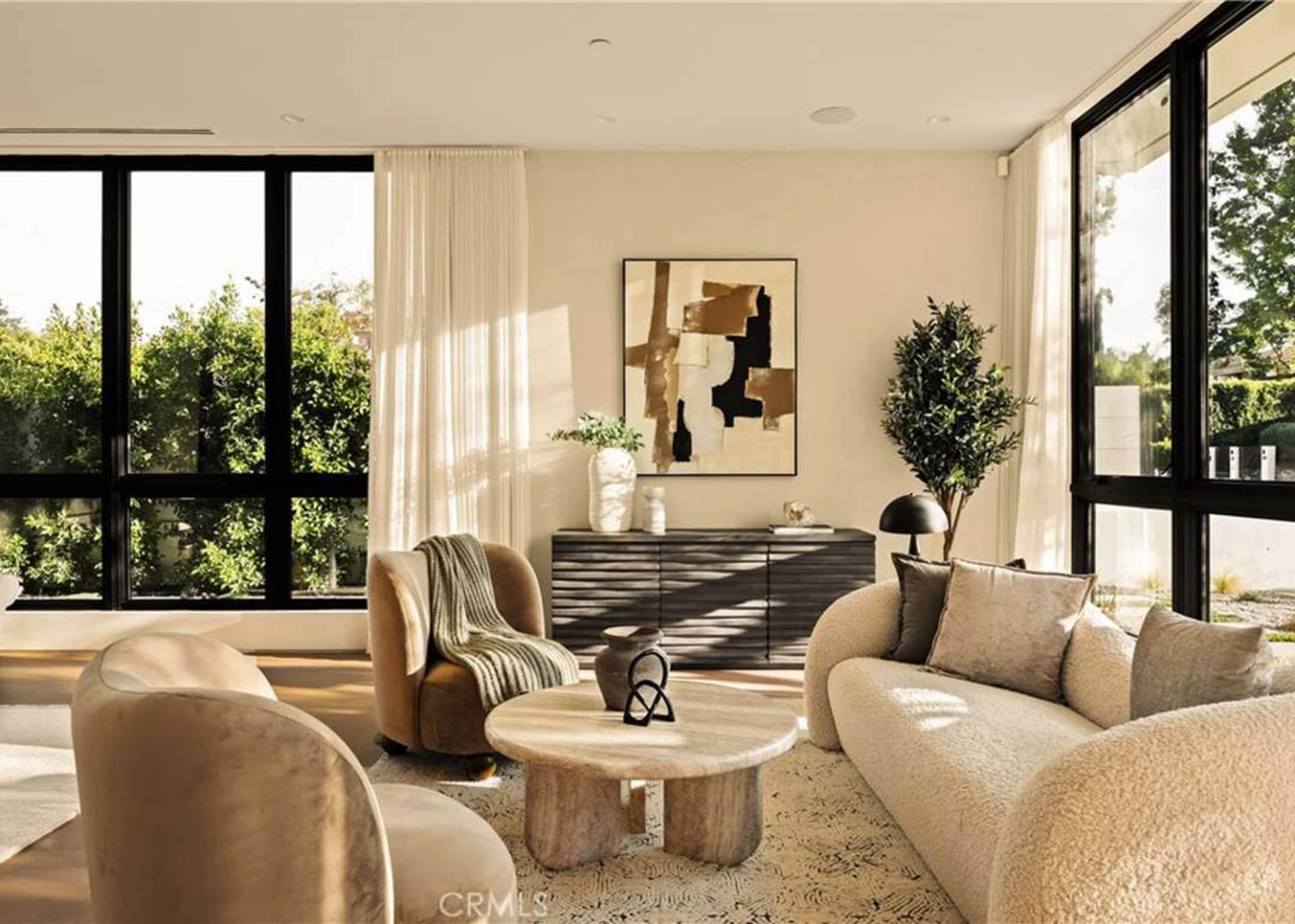 The image features a modern living room with large windows, a circular coffee table, and curved sofas arranged around it.
