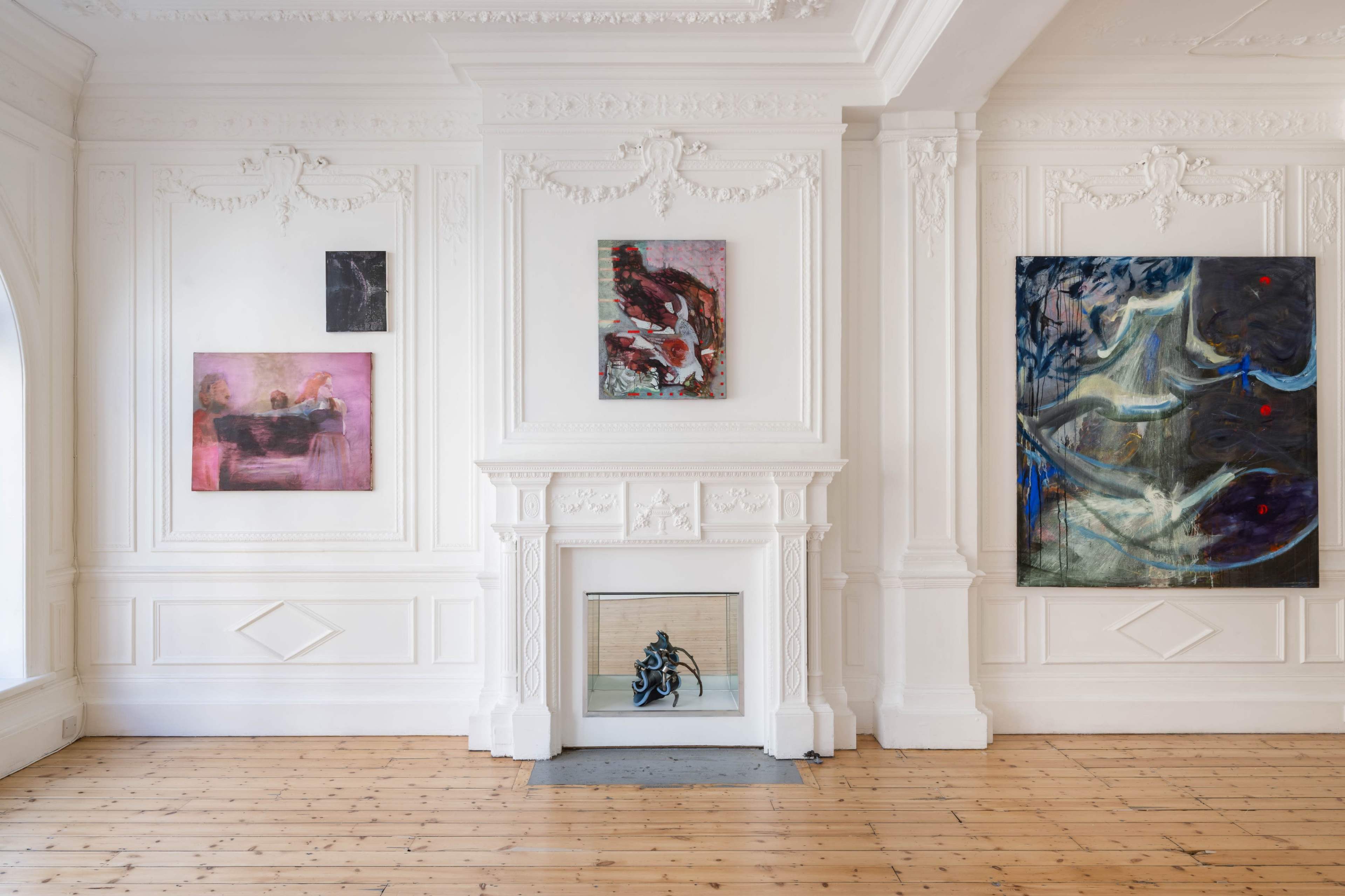 The scene features an art gallery with white walls displaying several paintings, including abstract and colorful artworks, around a central fireplace with a decorative mantel.