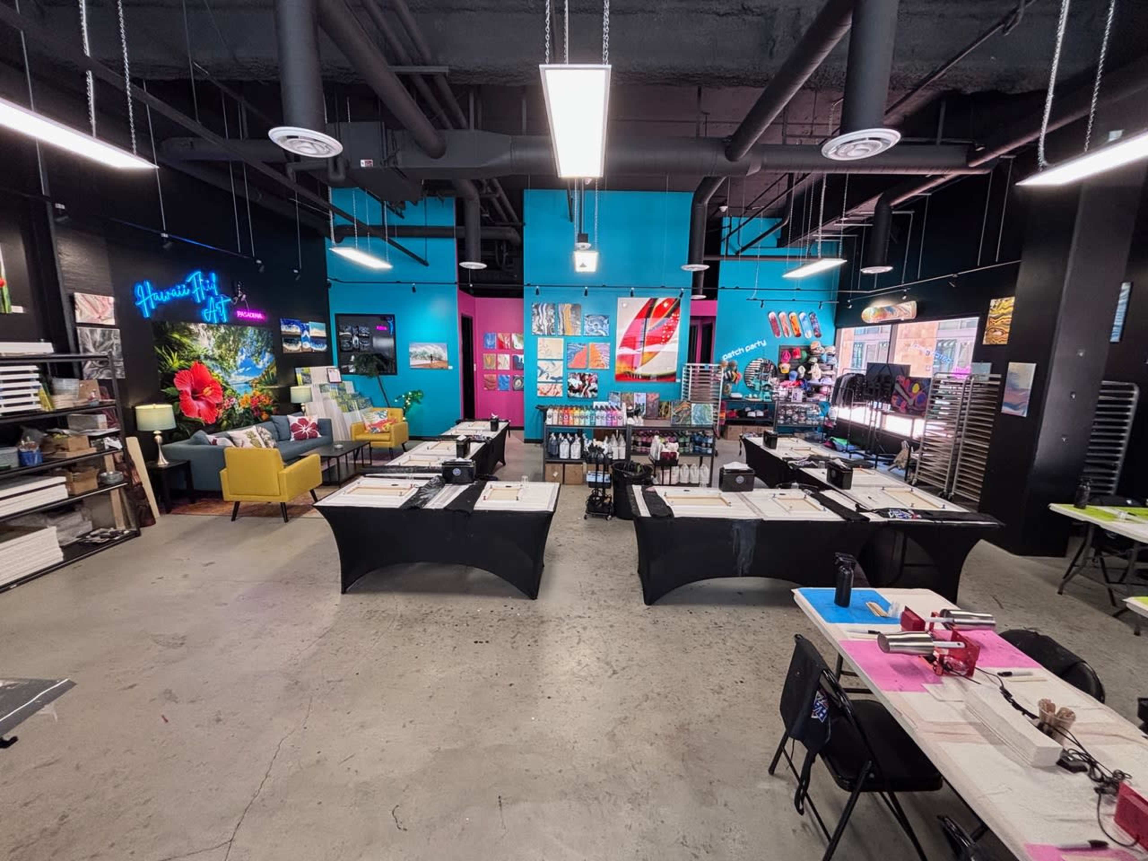The image shows a vibrant arts and crafts studio with multiple workstations arranged around the space, featuring colorful walls and various art supplies on display.