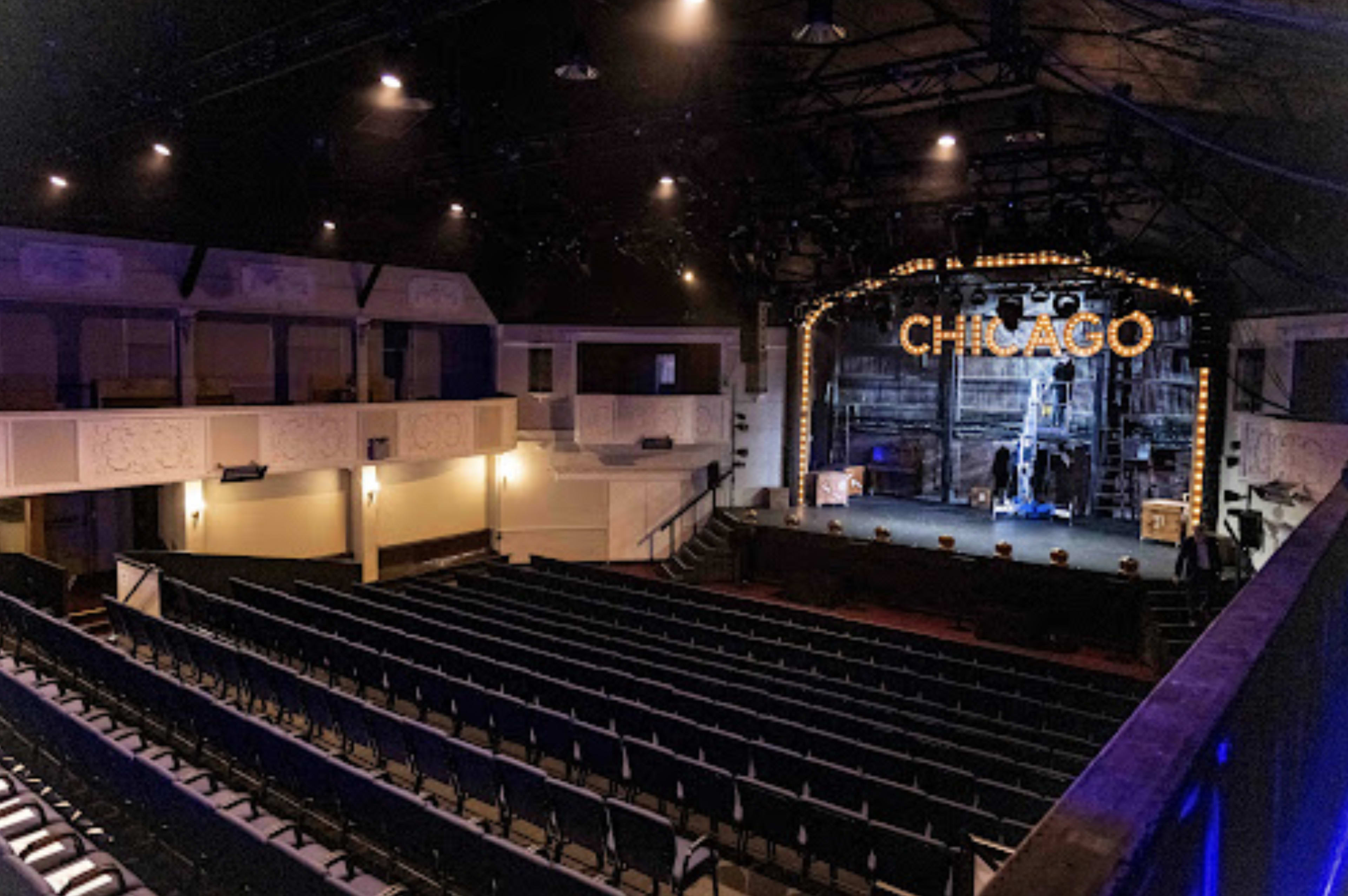 An empty theater with a stage labeled "CHICAGO," featuring rows of seats and a variety of stage lighting.