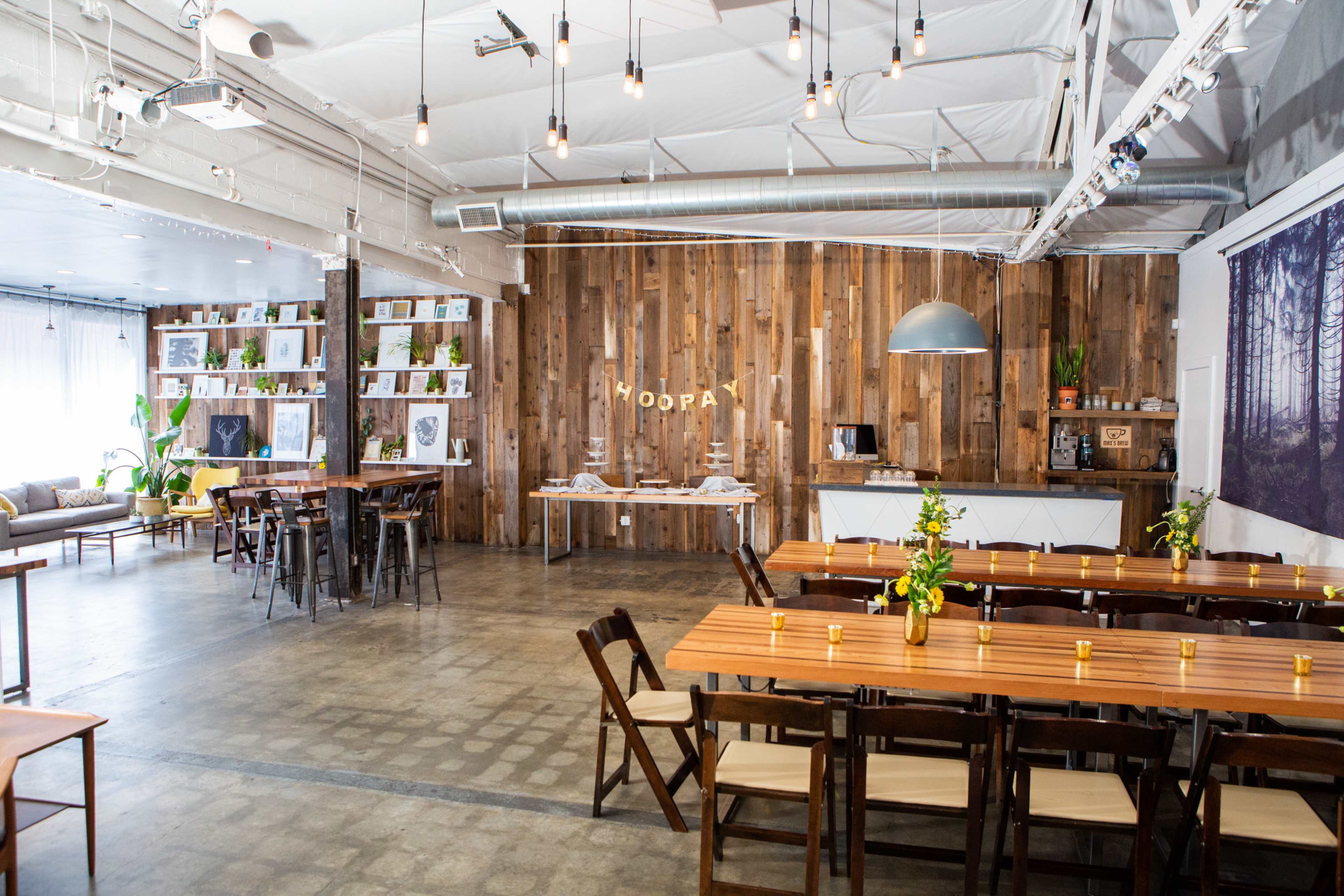 A spacious interior of an event space with wooden tables, chairs, and a rustic wooden accent wall featuring the word "HOOPLA."