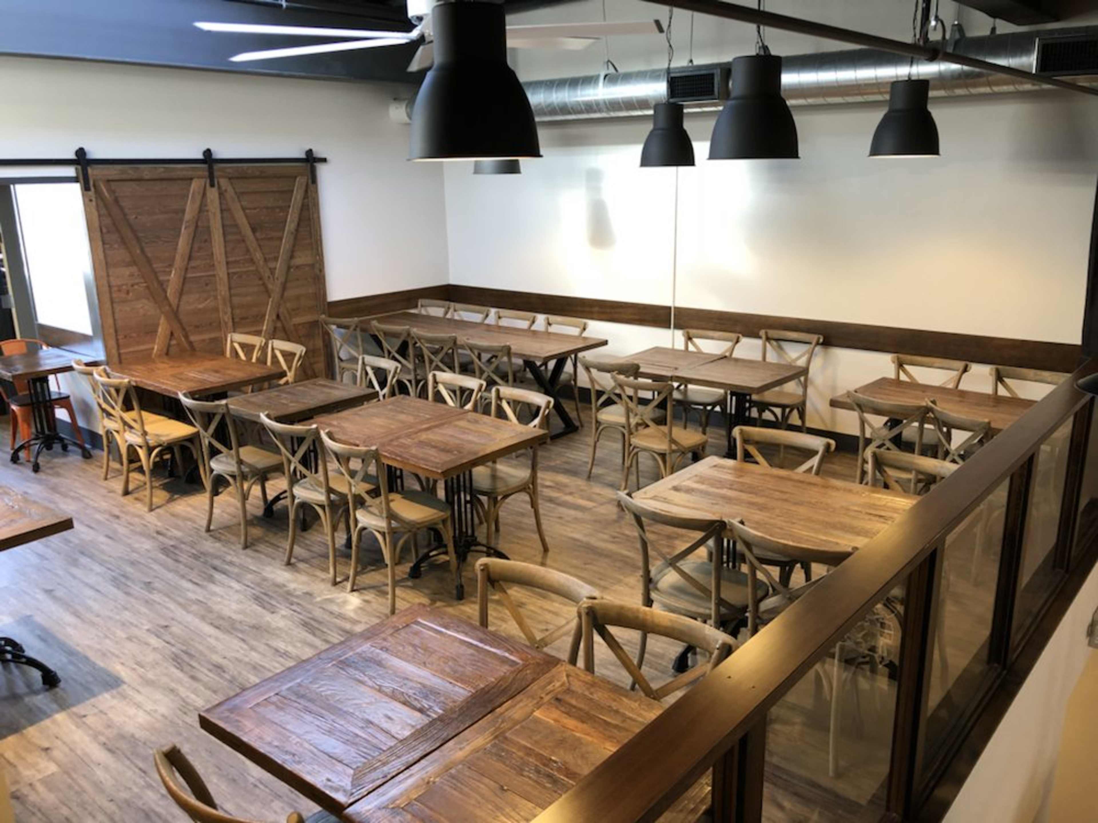 A spacious restaurant interior with wooden tables and chairs arranged neatly in multiple sections.