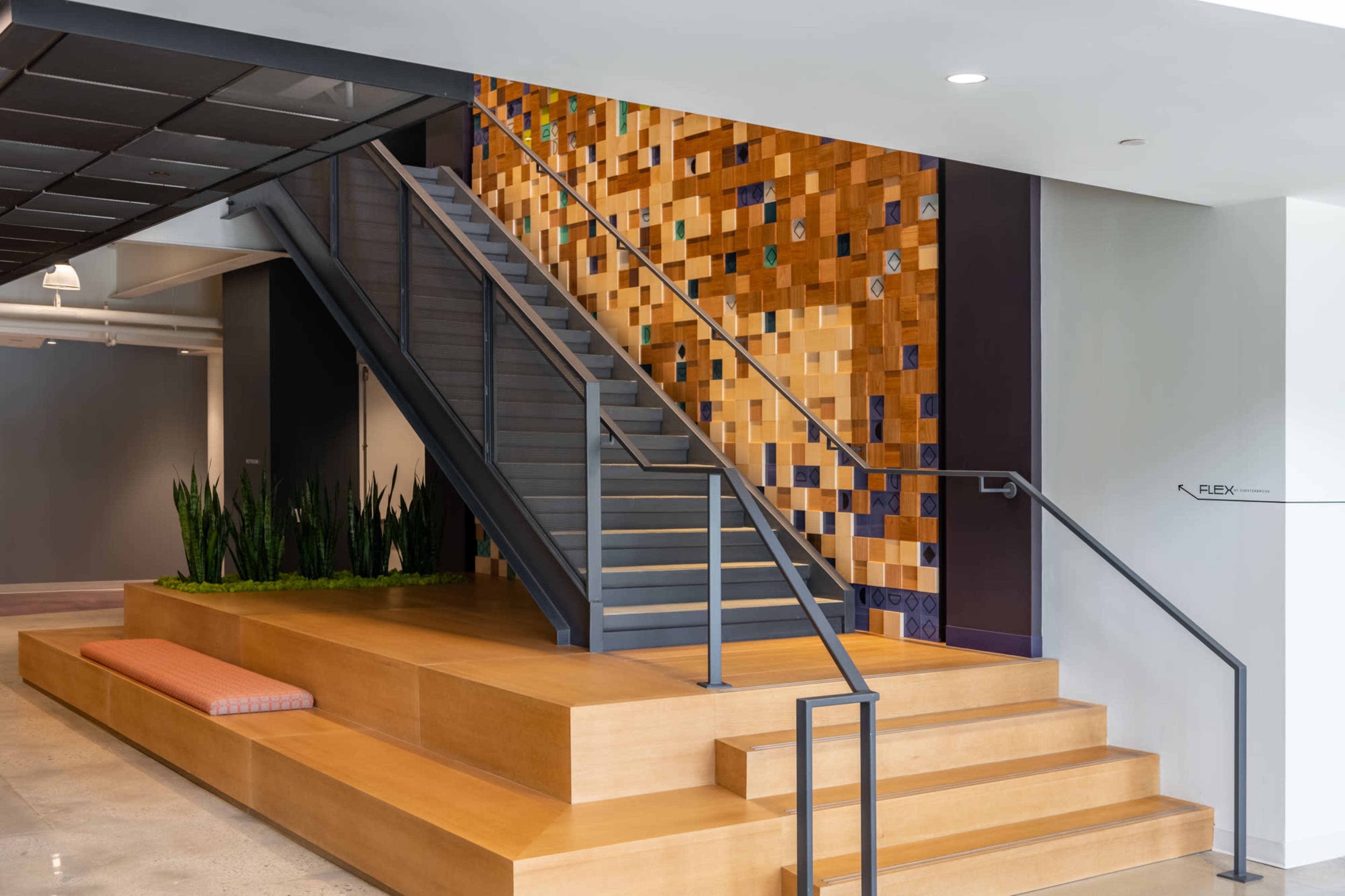 A modern staircase leading to an upper level, with a colorful tiled wall and a wooden platform that includes seating.