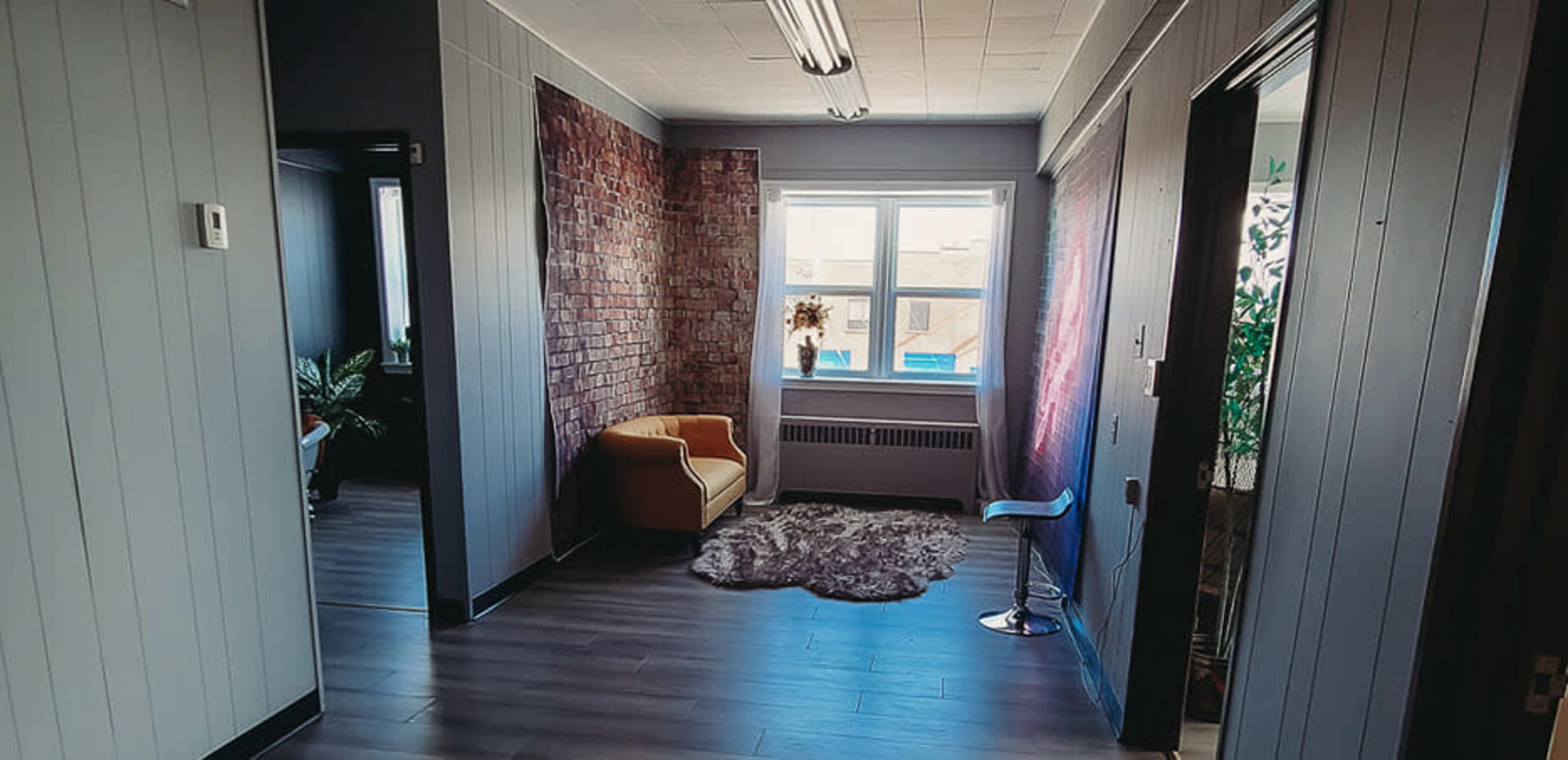 A hallway with a brick feature wall, a yellow armchair, and a window facing the outside.