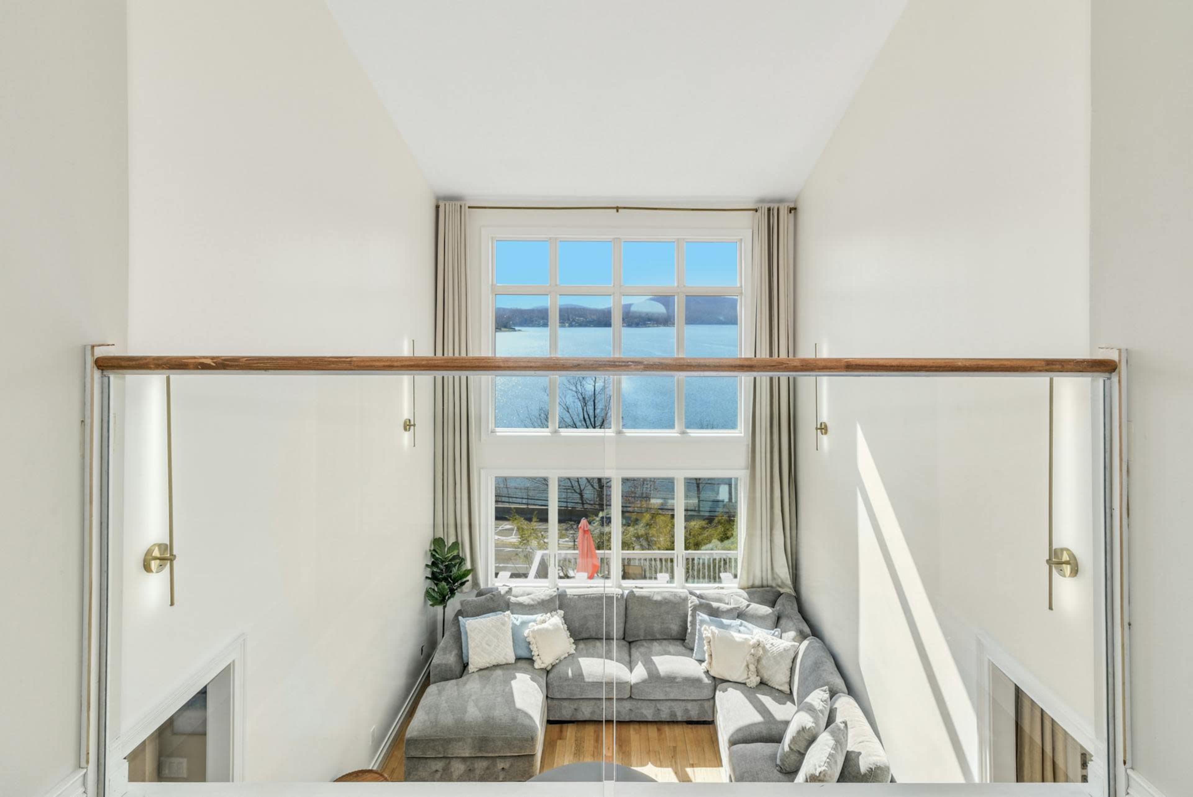 A spacious living area features a large gray sectional sofa and a large window offering a view of the lake.