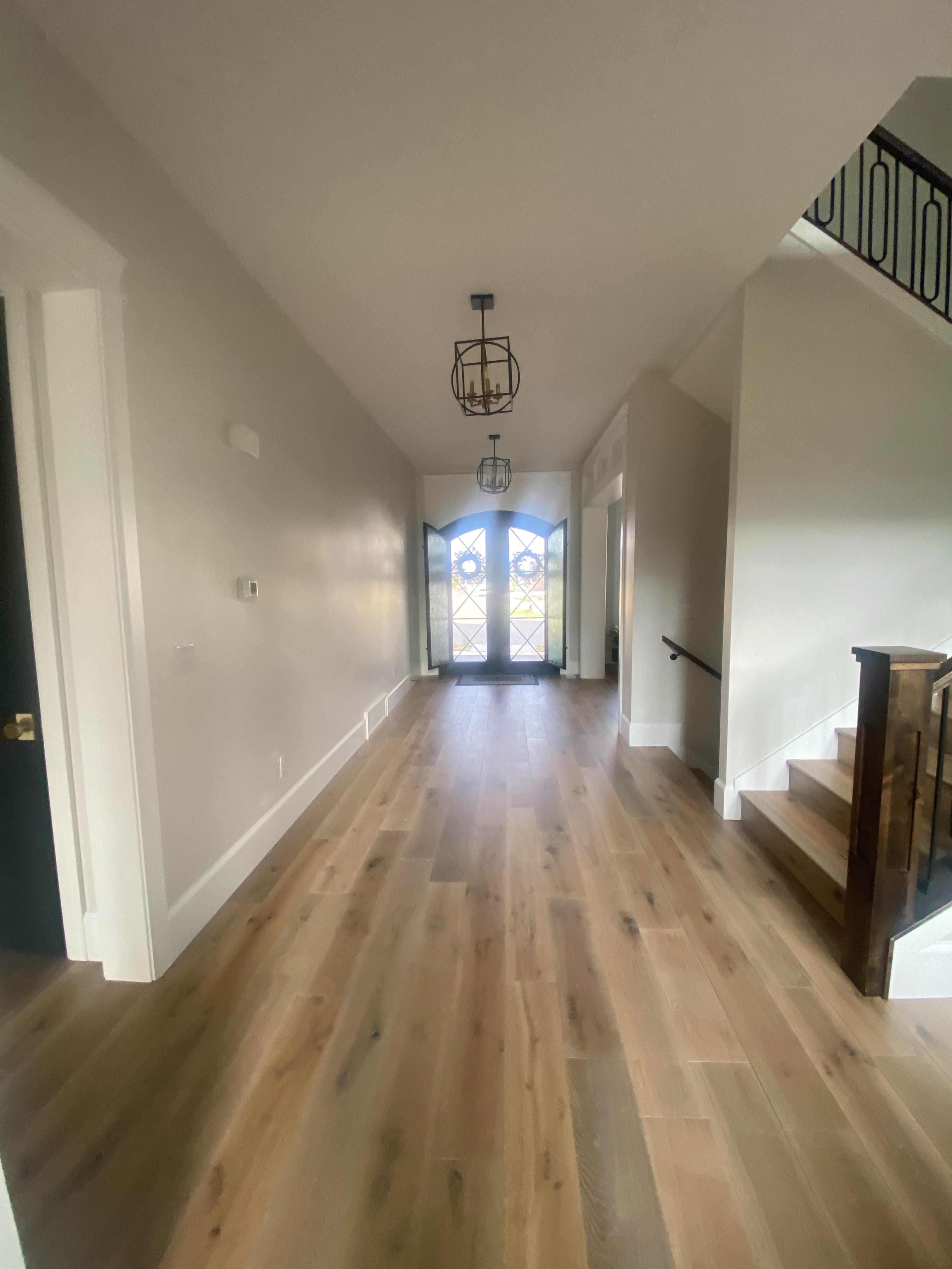 A spacious hallway features wooden flooring leading to double doors with window panels, flanked by a staircase on the right.