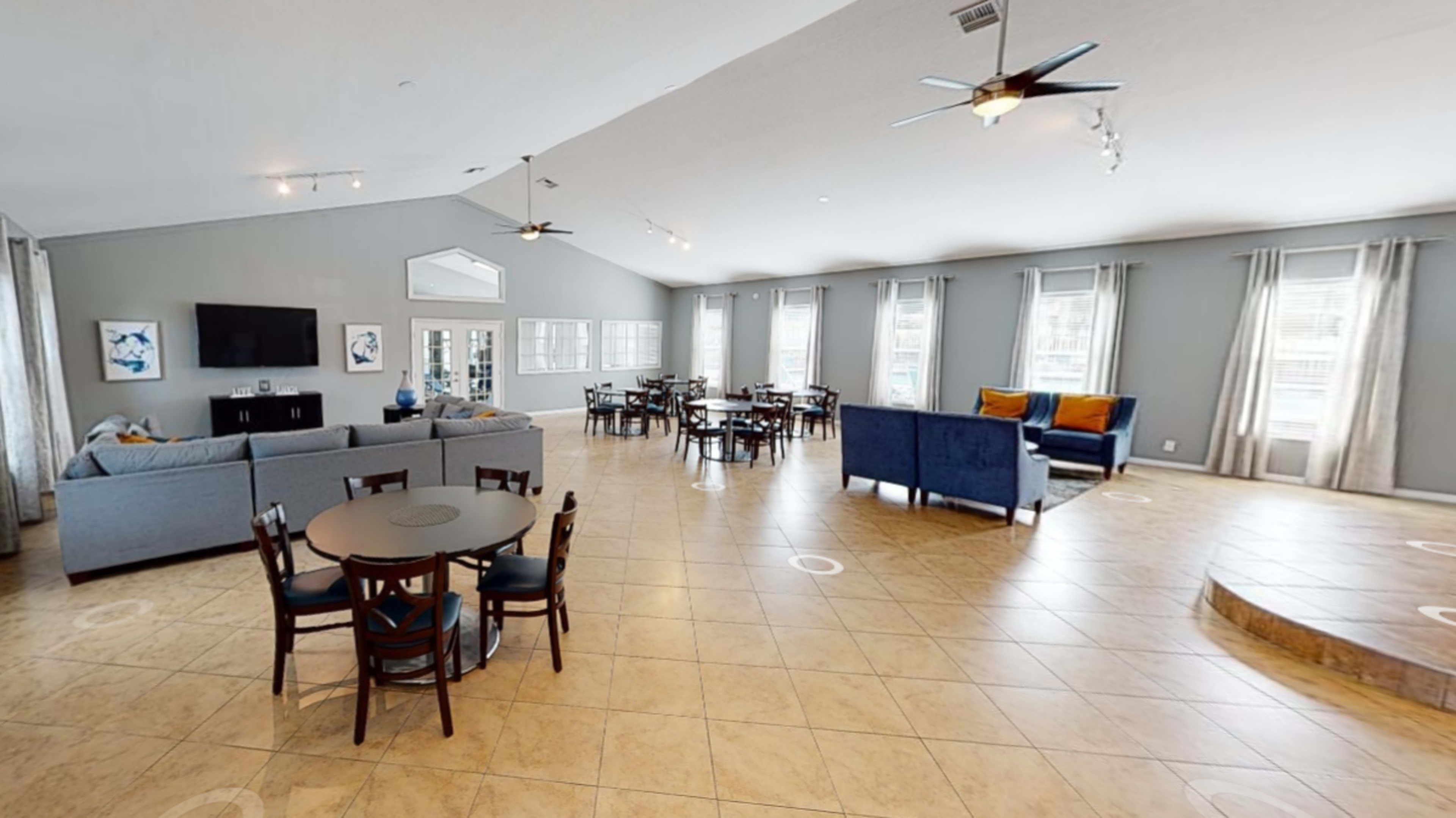 A spacious common area with multiple seating arrangements, including sofas and tables, illuminated by natural light through large windows.